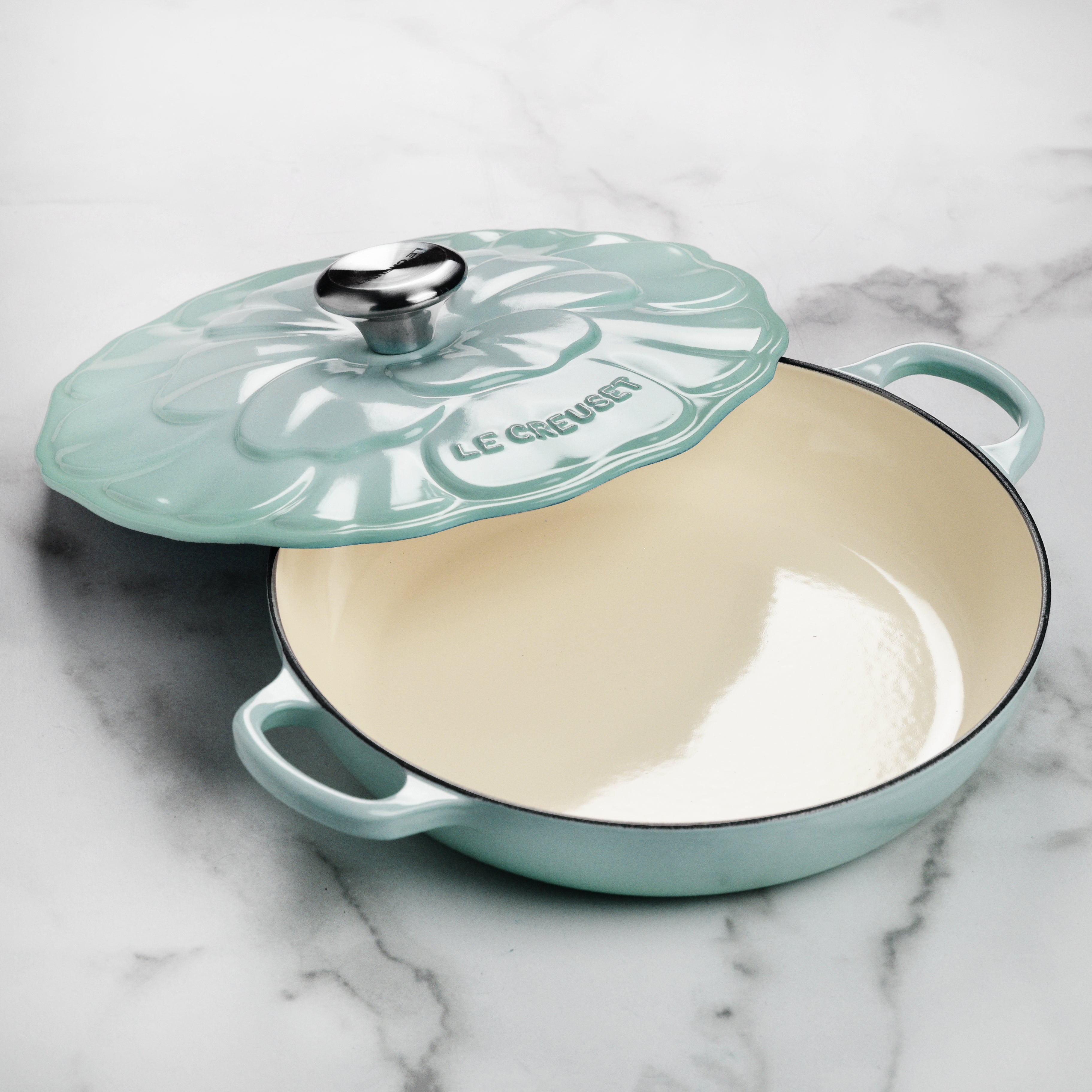 Side view of Sea Salt Petal Enameled Cast Iron Braiser with lid on a stove.