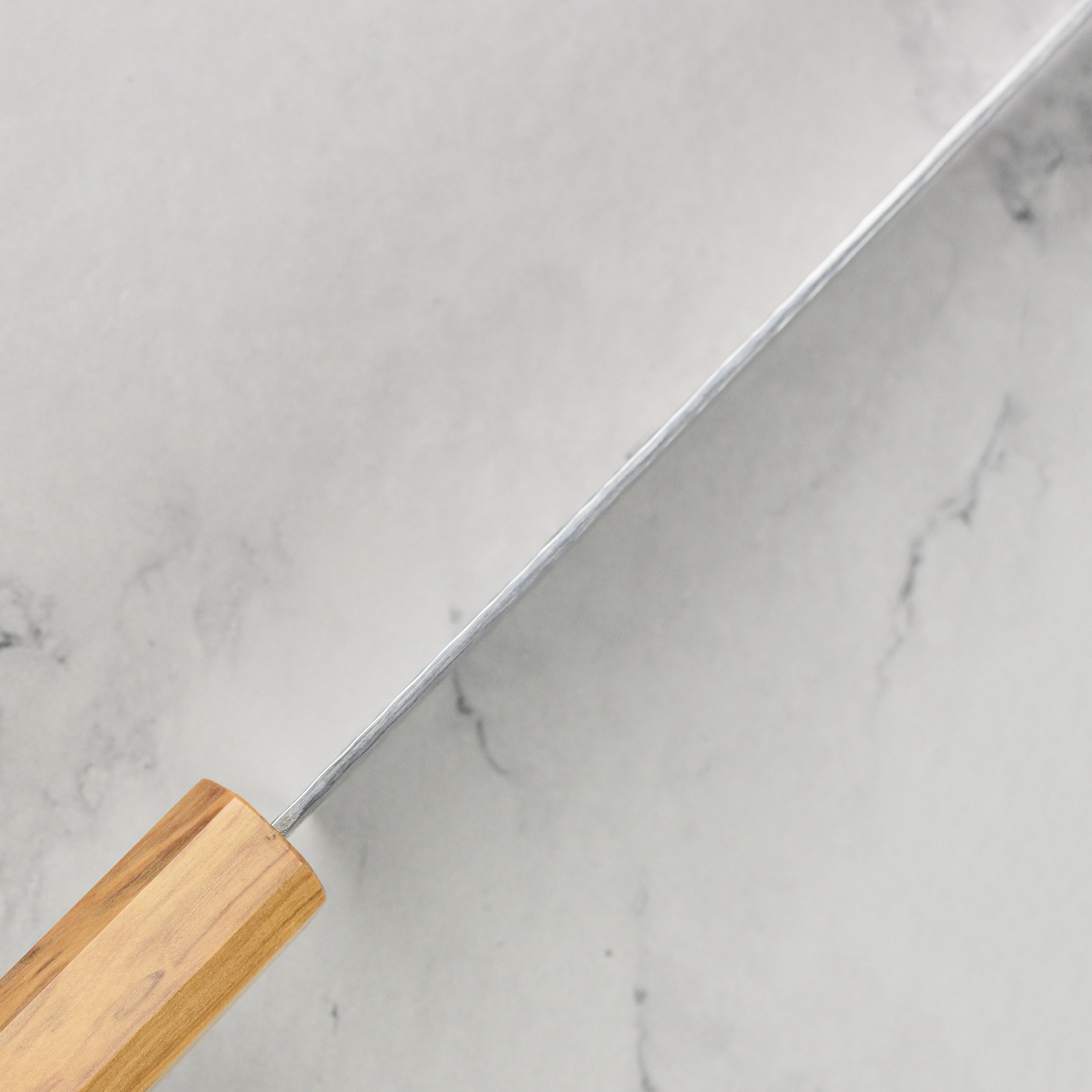 Close-up of Japanese chef knife blade and olivewood handle with detailed craftsmanship