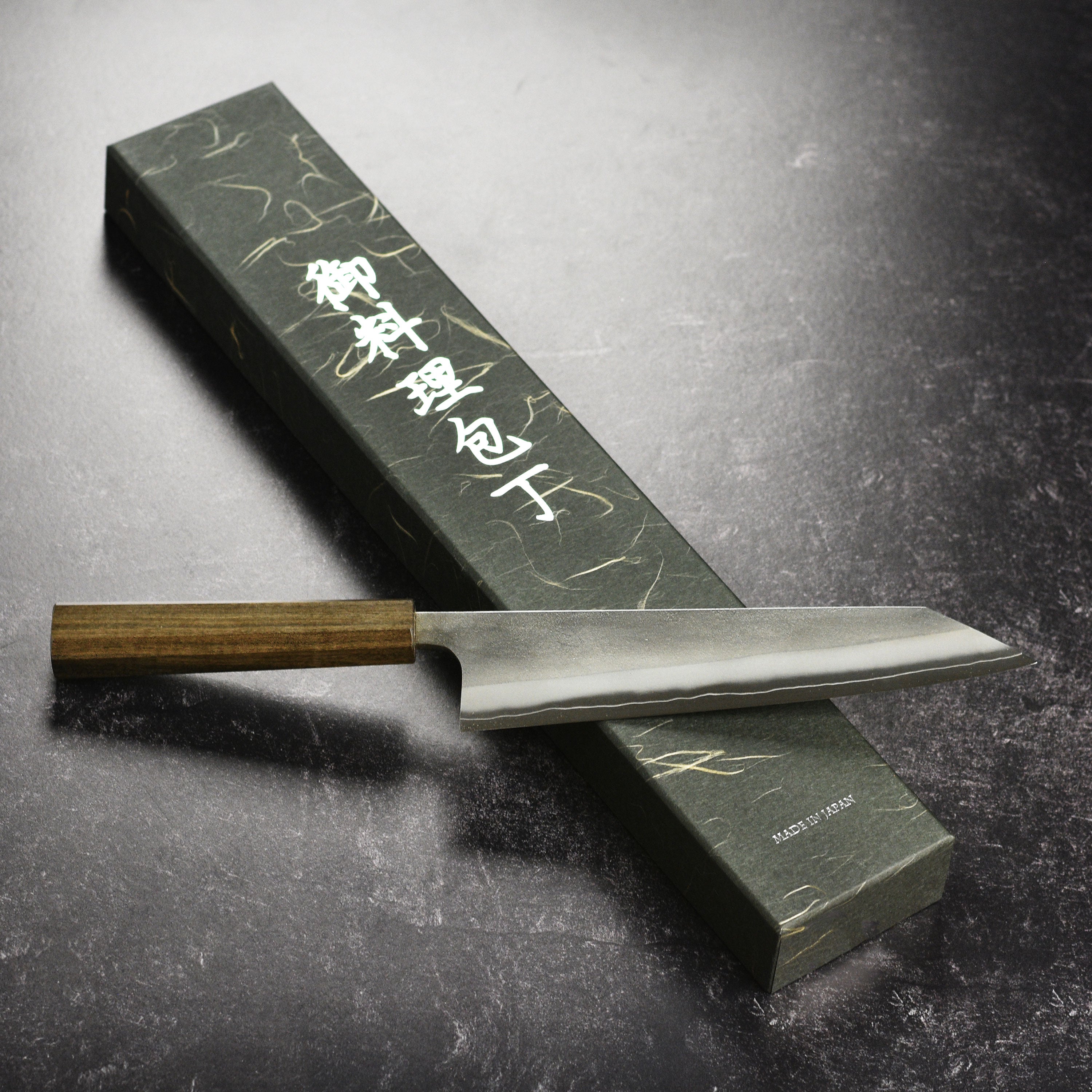 Yoshikane Kiritsuke knife displayed next to a cutting board and fresh ingredients.