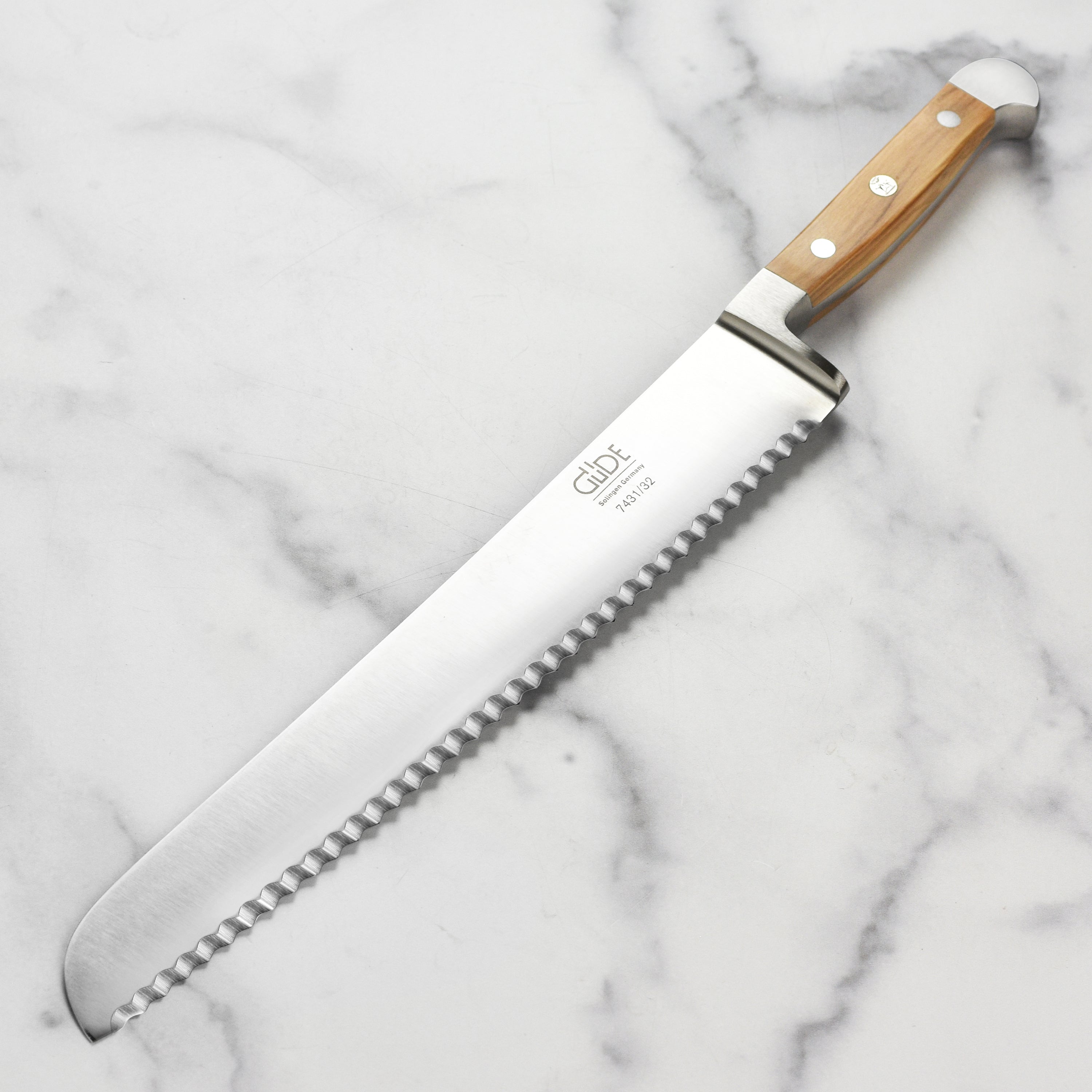 Close-up of Franz Gude 12.6-inch bread knife with olive wood handle, showing serrated edge for crusty bread