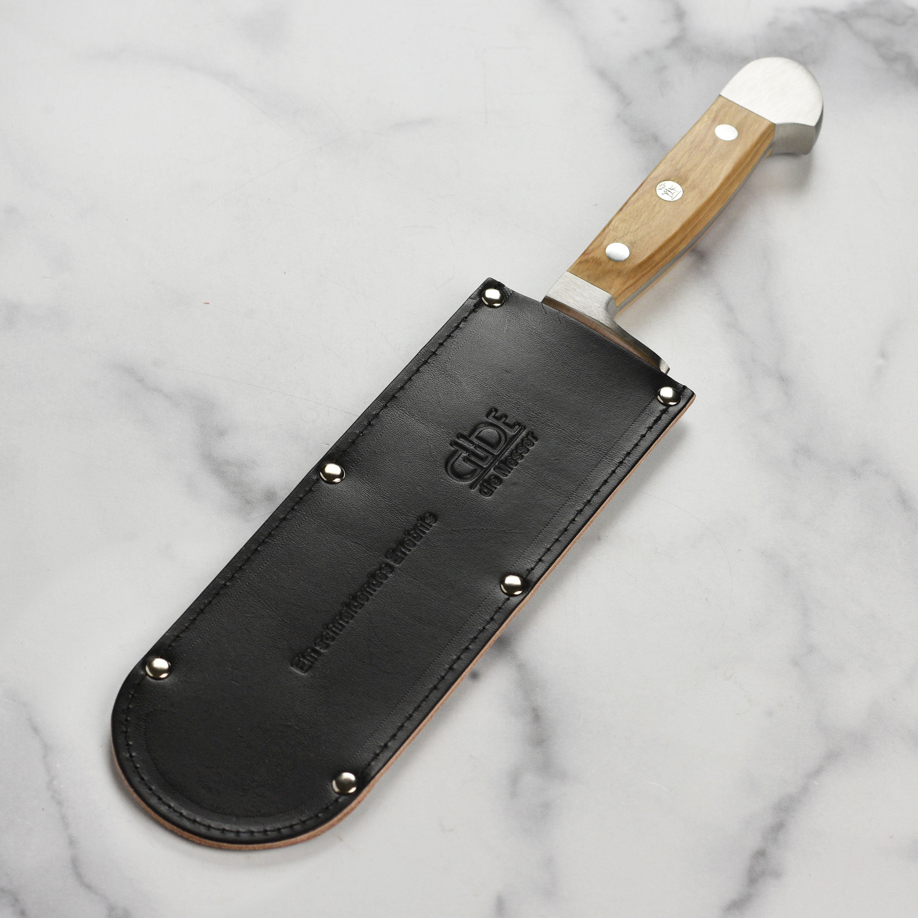 Chef knife inserted halfway into cowhide sheath on drawer edge