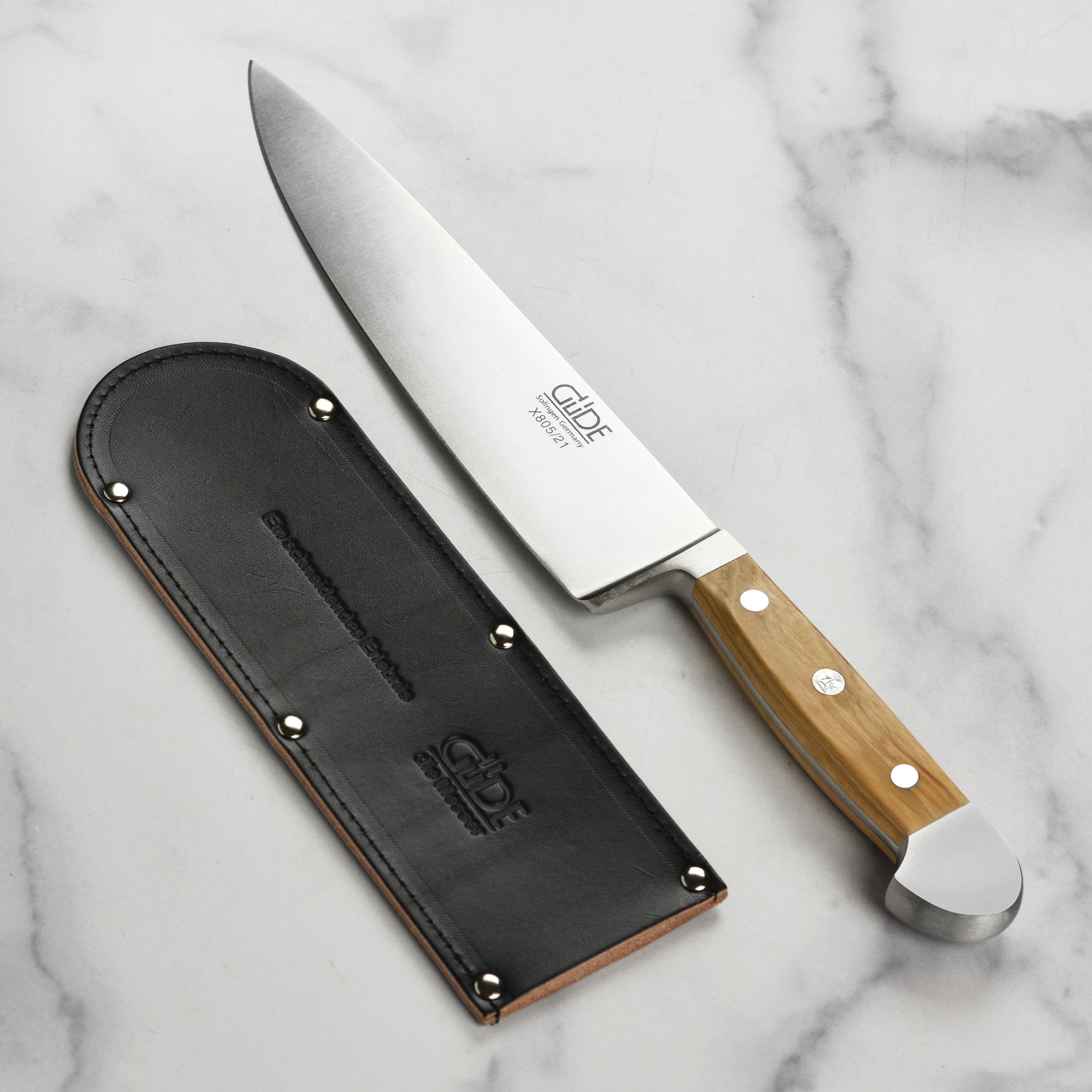 Chef knife inserted halfway into cowhide sheath on drawer edge