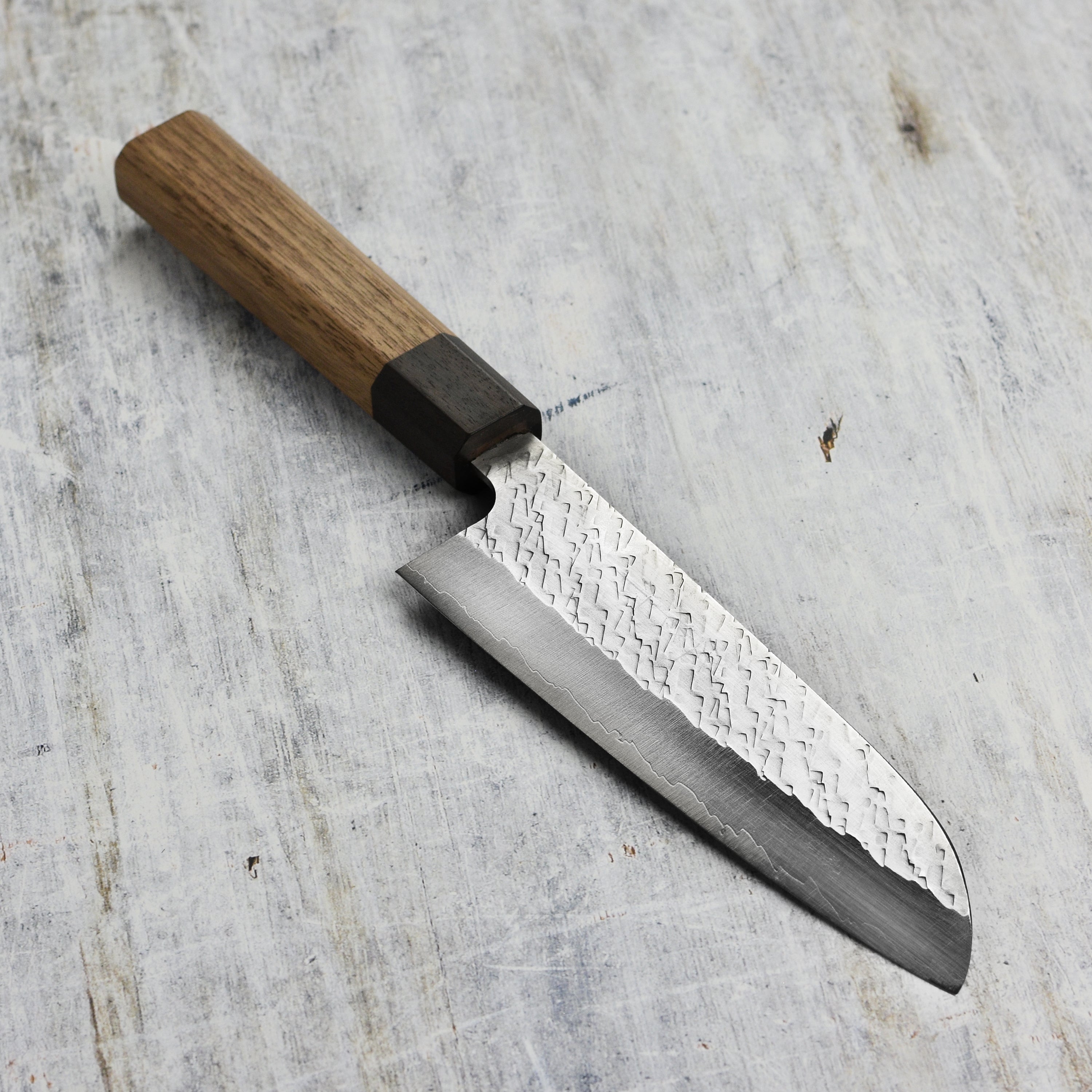 Close-up of SPG STRIX santoku knife blade showing hammered tsuchime texture and polished finish
