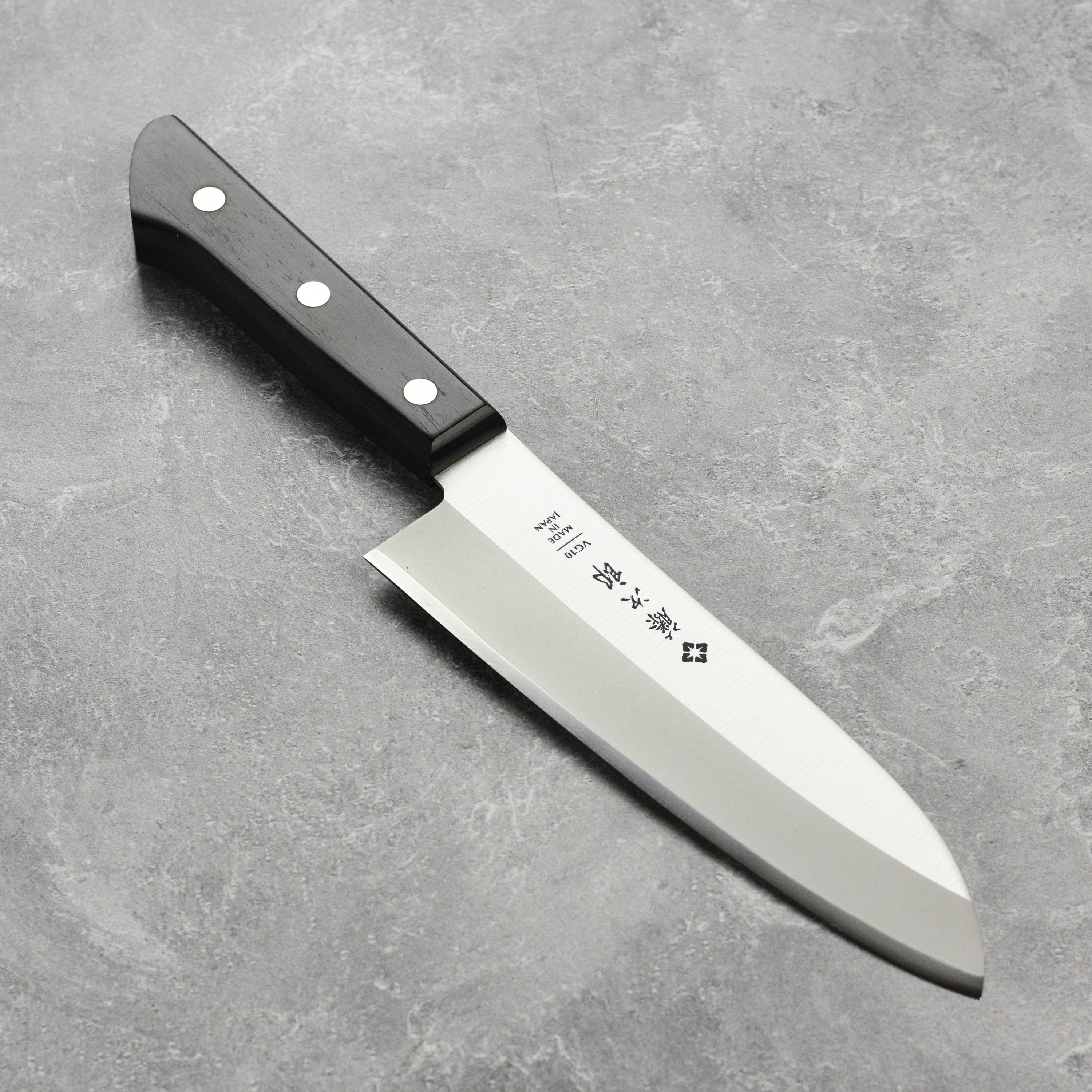 Tojiro VG-10 Santoku knife angled view on a wooden cutting board, highlighting its sharp blade and Pakkawood handle.