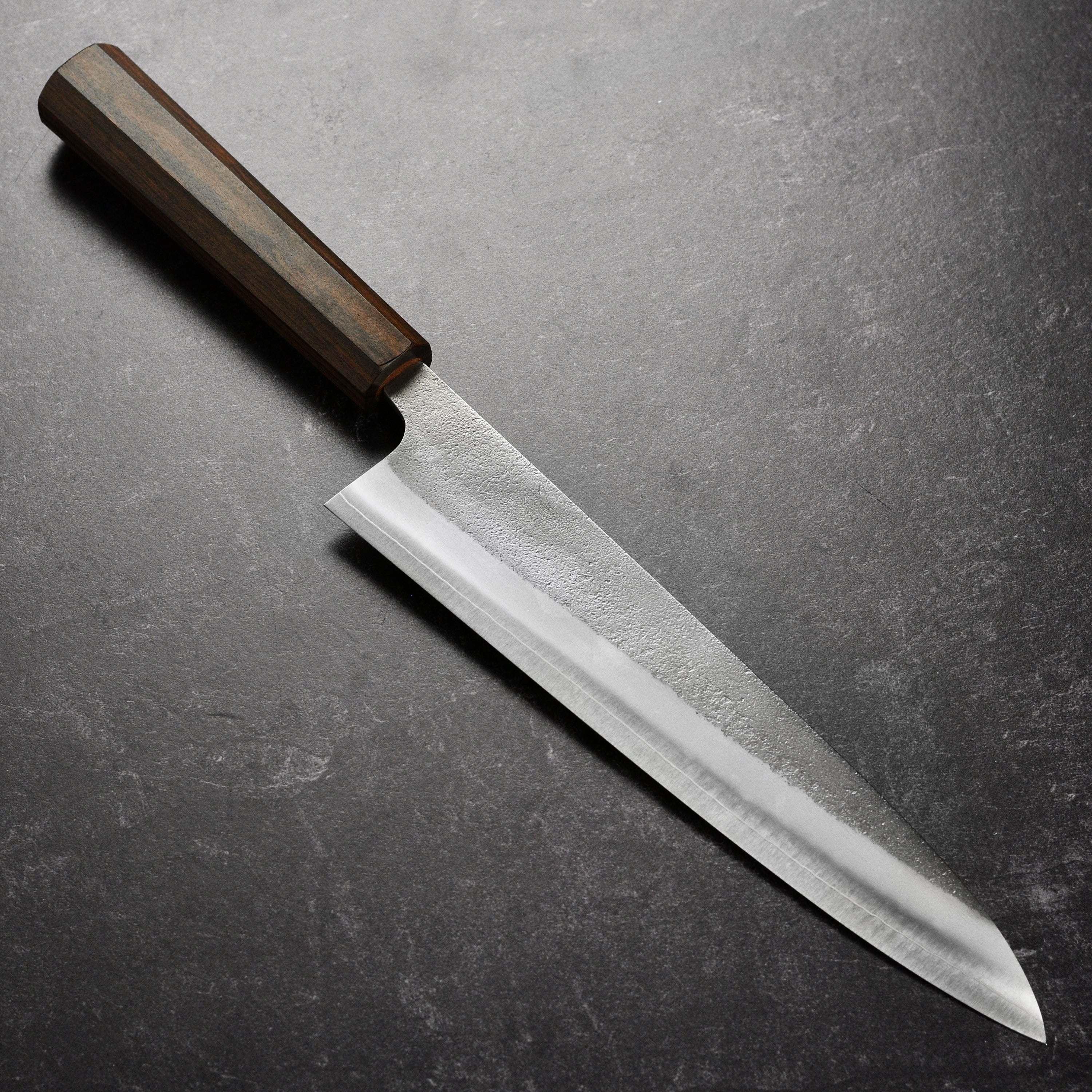 Yoshikane SKD Nashiji Gyuto Knife from a side angle, highlighting its sharp blade and sleek design.