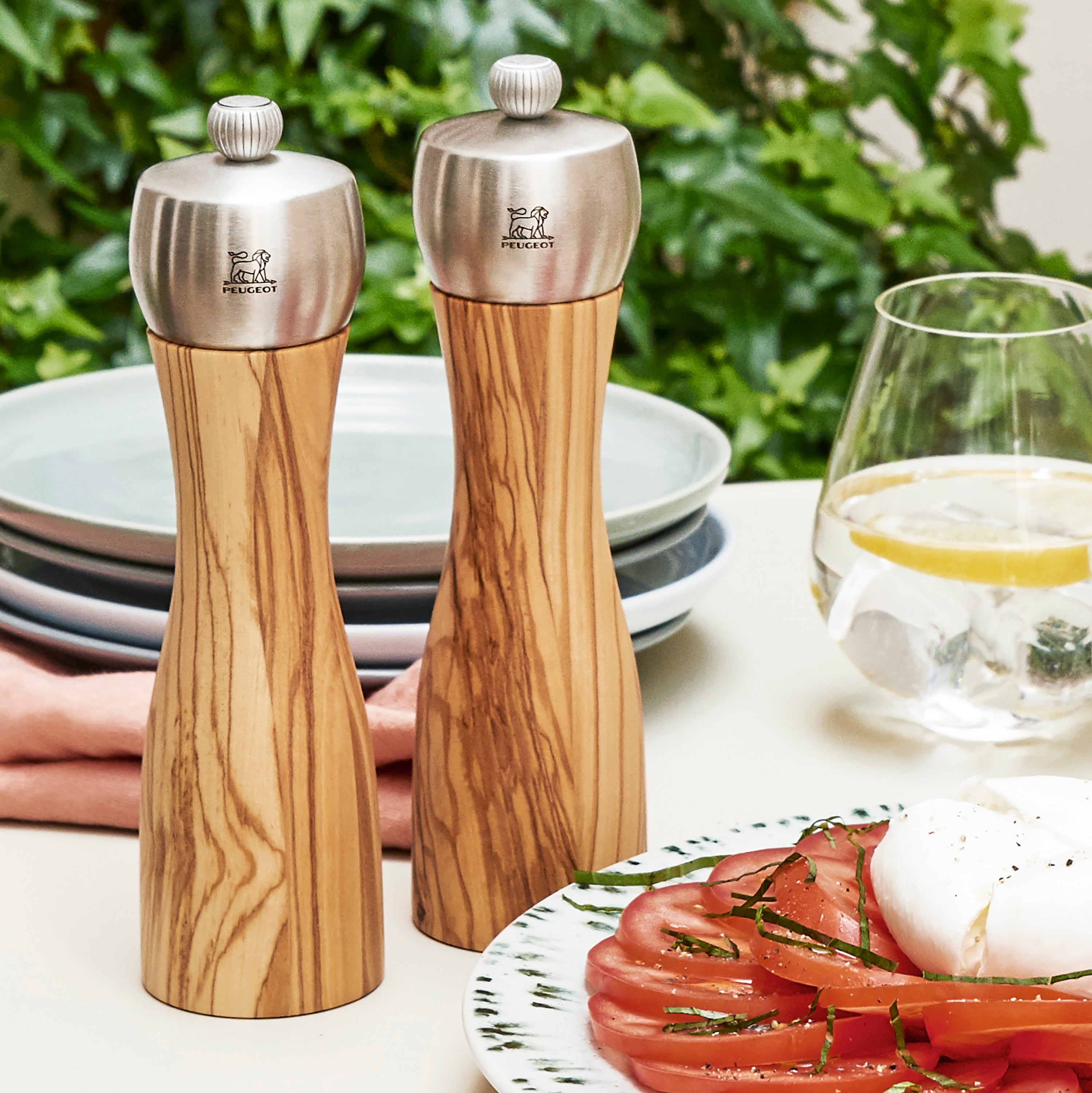 Peugeot Fidji Olivewood Salt and Pepper Mill Set on a dining table next to delicious food