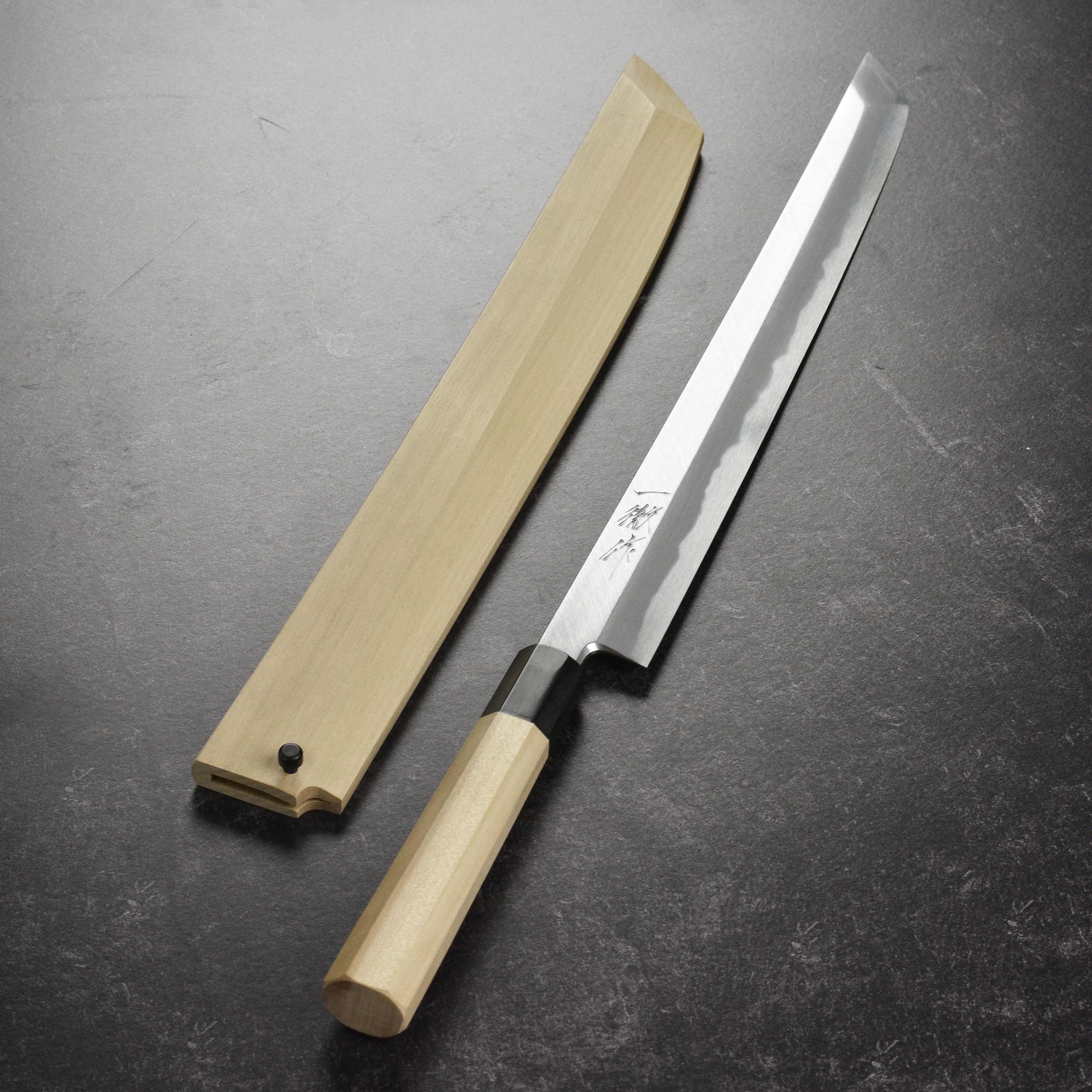 Affordable Takohiki knife with saya resting on a wooden cutting board, ideal for professional chefs.