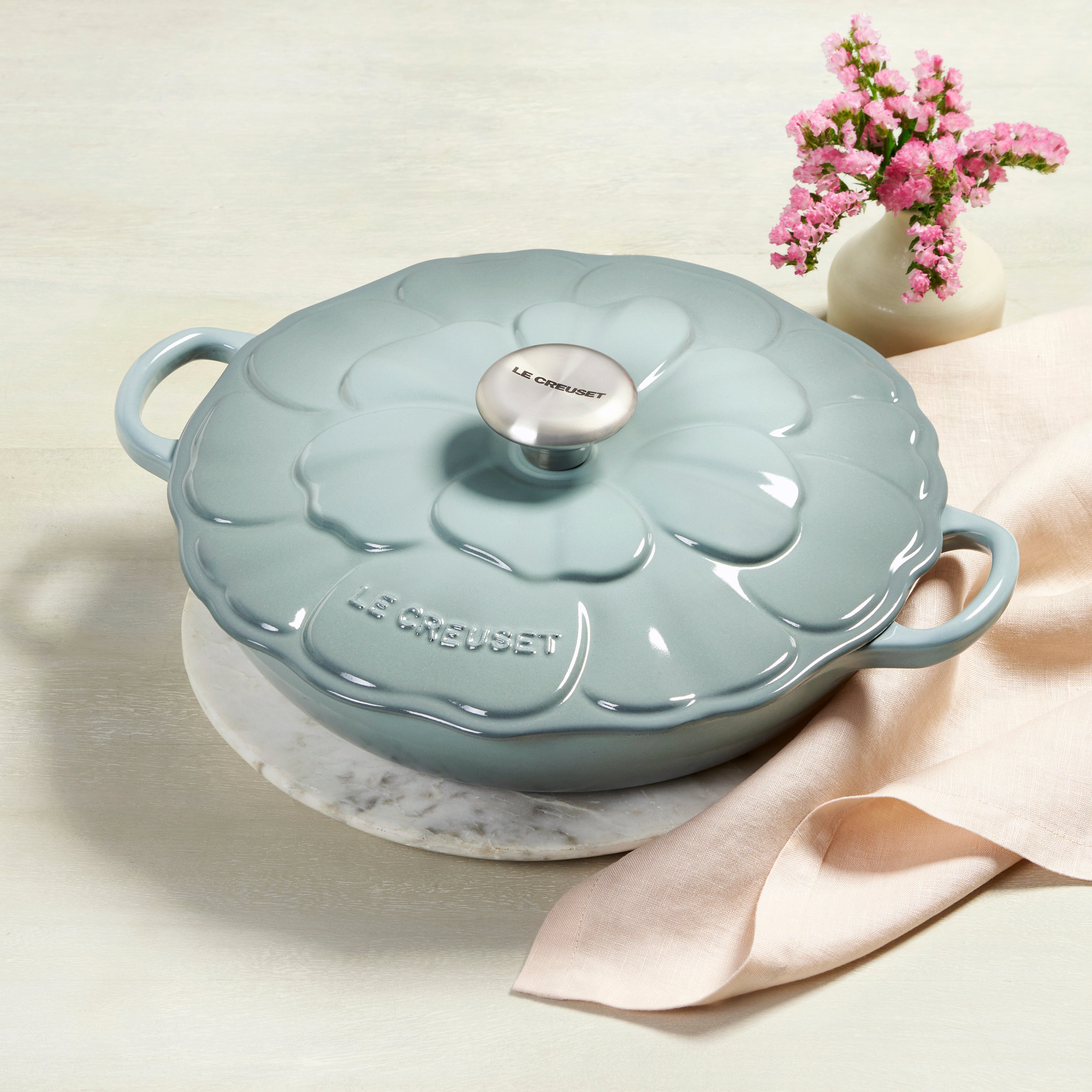 Side view of Sea Salt Petal Enameled Cast Iron Braiser with lid on a stove.