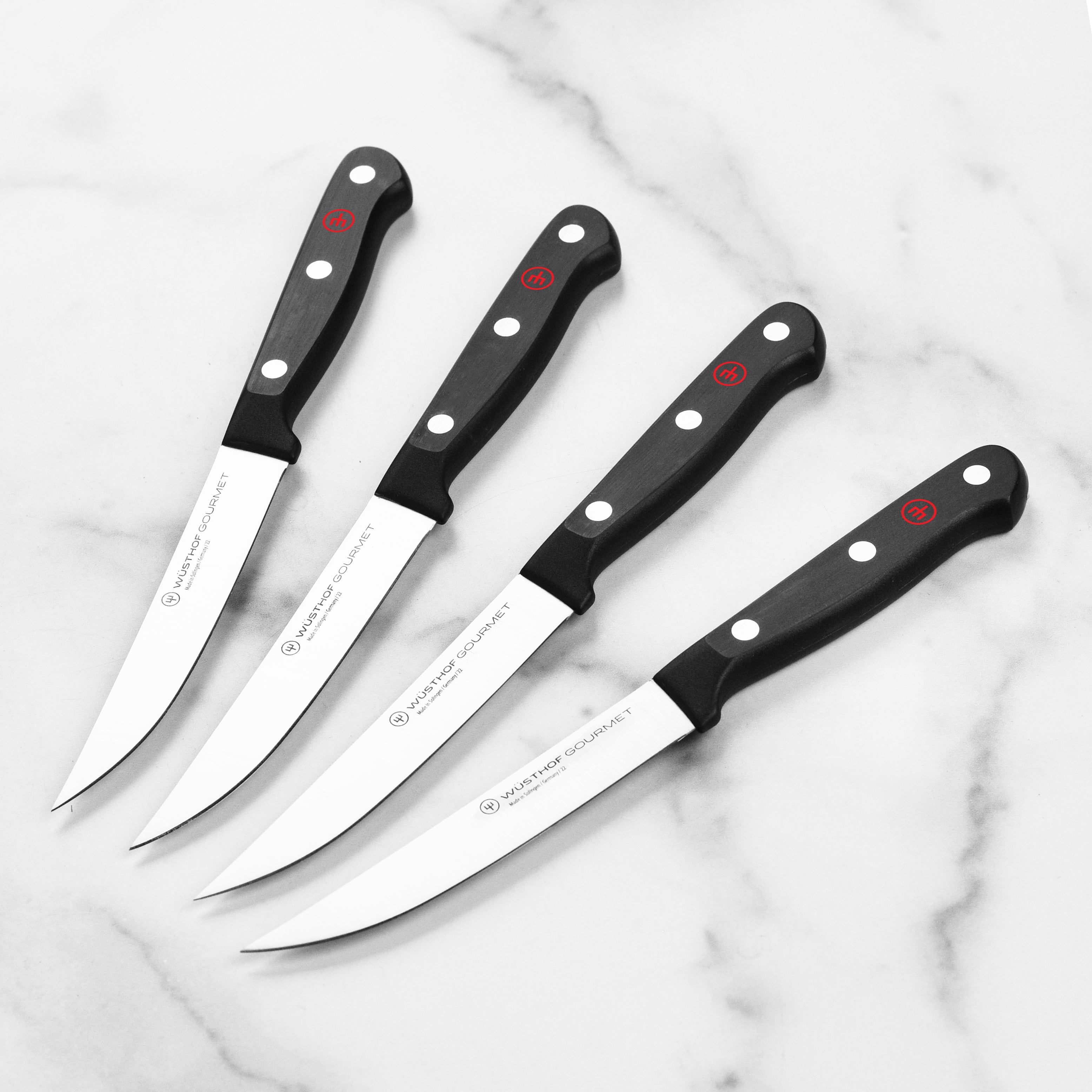 Close-up of Wusthof Gourmet steak knives on a wood cutting board, showcasing sharp blade edges and triple-riveted handles.