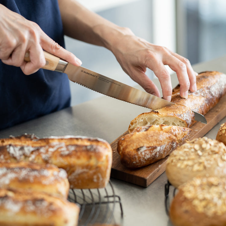 Suncraft Seseragi bread knife displayed on a wooden cutting board with fresh tomatoes.
