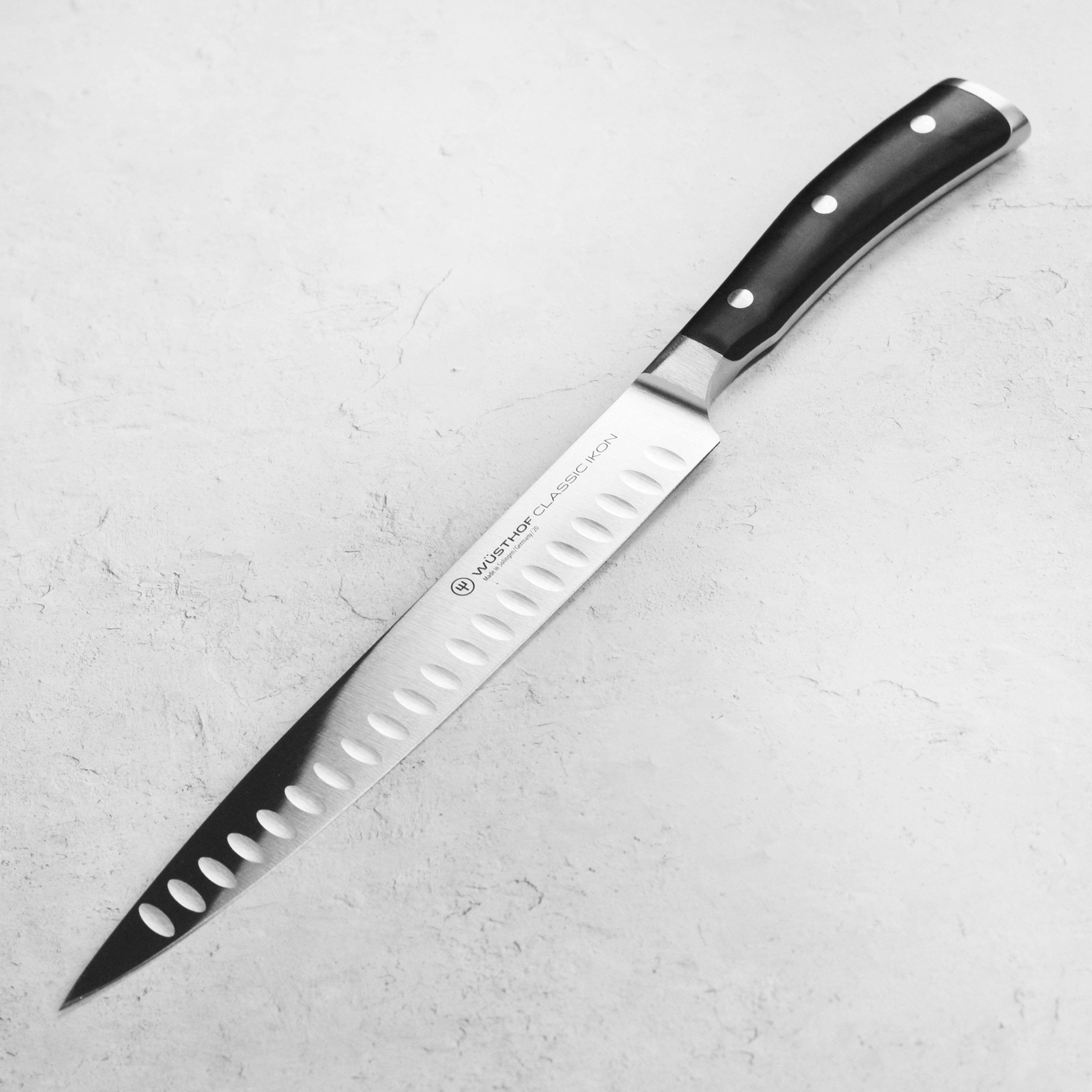 A top-down view of the Wusthof Classic Ikon carving knife showing its hollow edge design on a walnut cutting board.