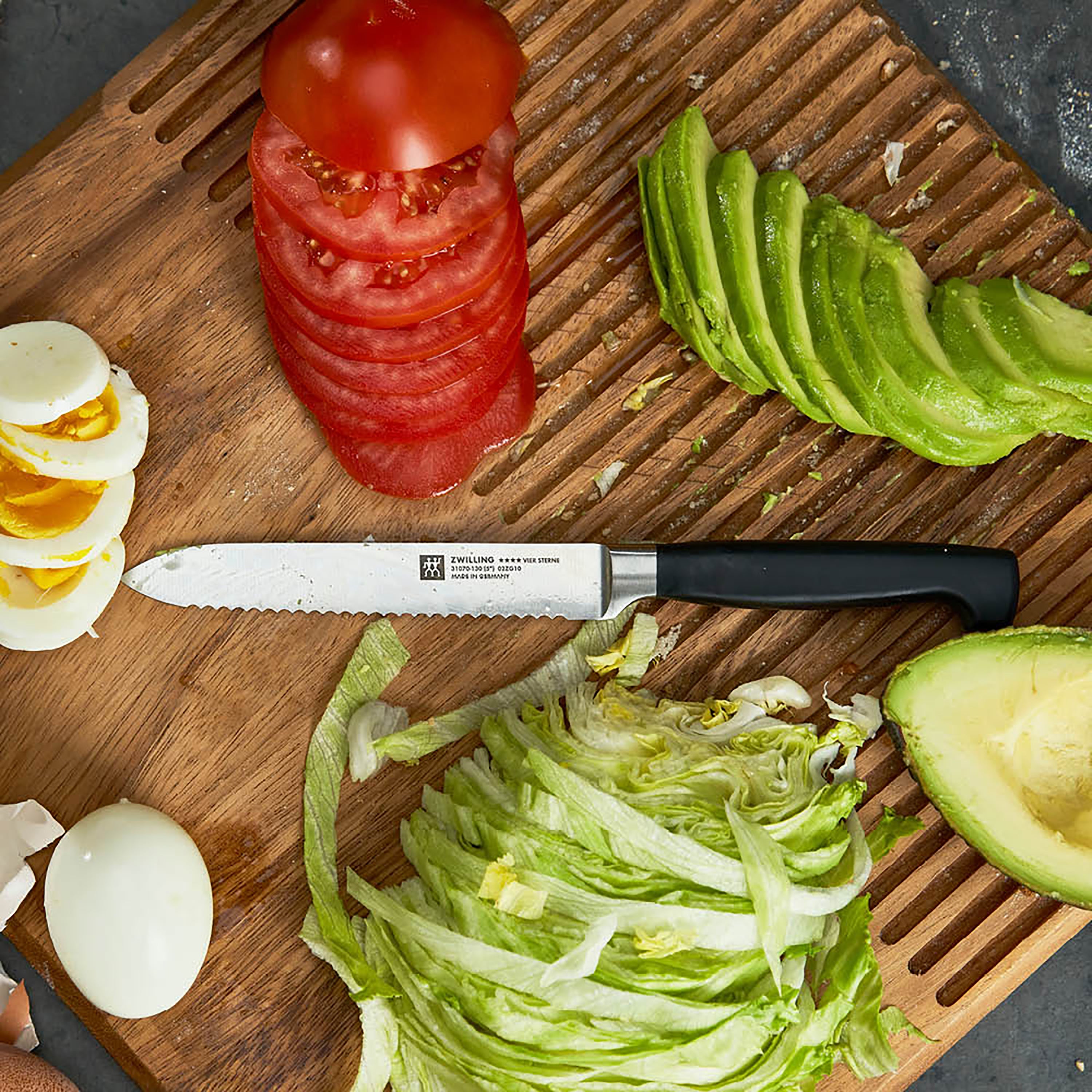 Close-up of Zwilling Four Star 5" serrated utility knife on a wooden cutting board, demonstrating its sharpness and craftsmanship.