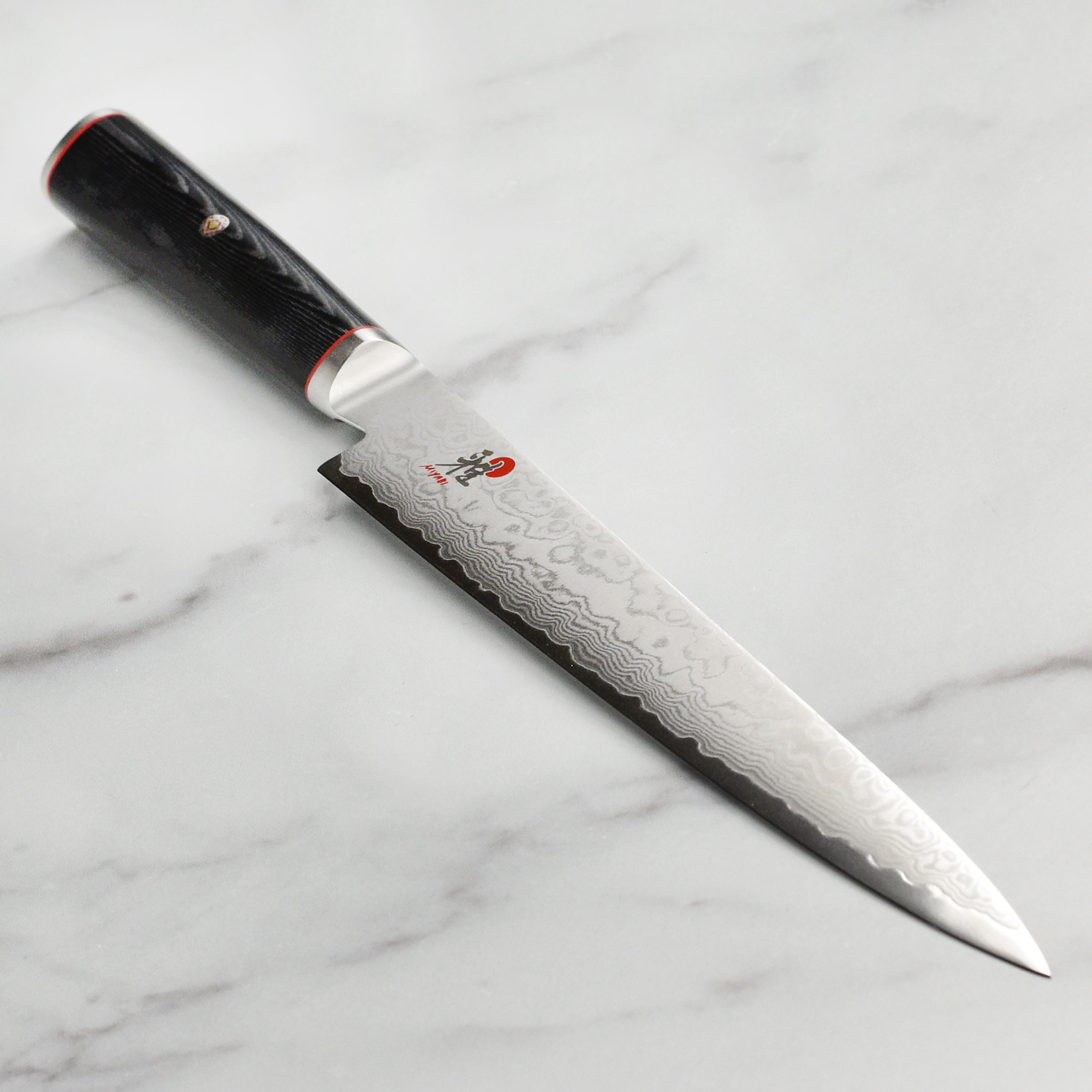 Close-up of the Miyabi Kaizen slicing knife showcasing the Damascus steel pattern and sharp edge.