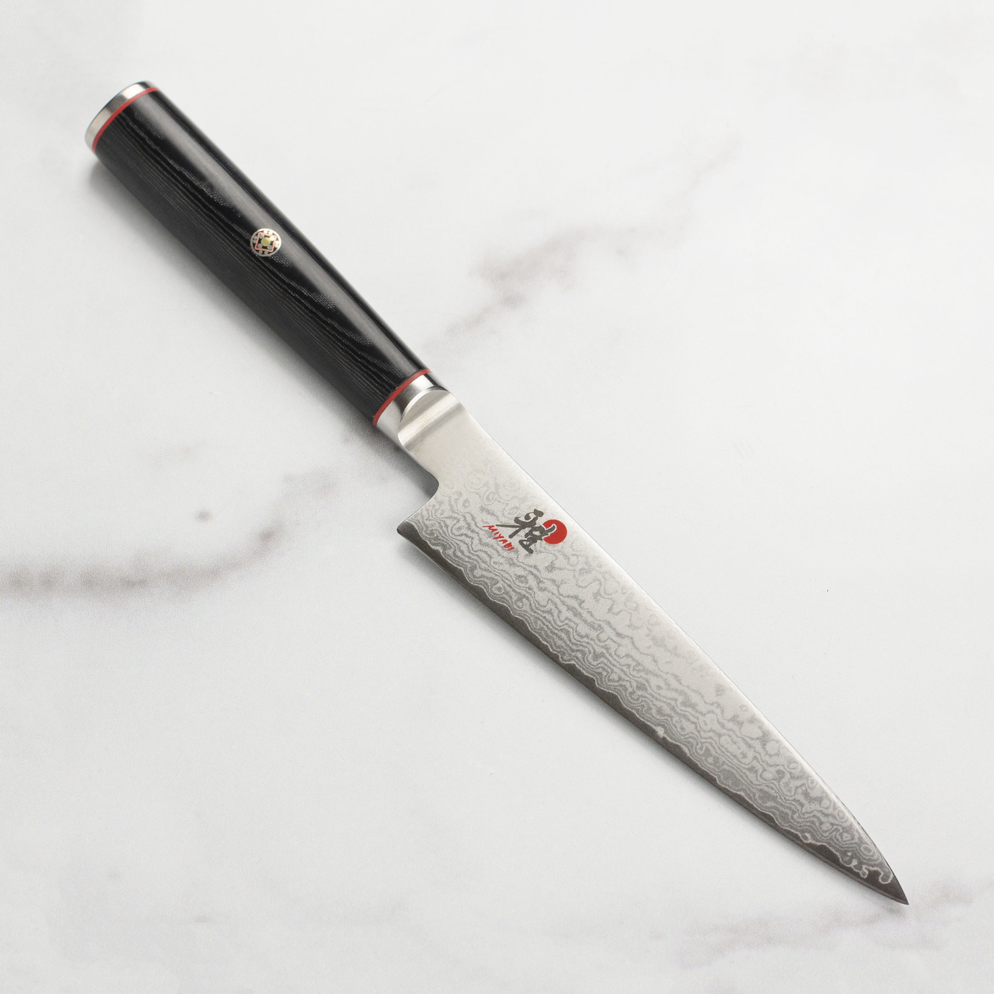 Close-up of the Seki Artisan Damascus utility knife showcasing the intricate Damascus pattern and VG10 steel blade.
