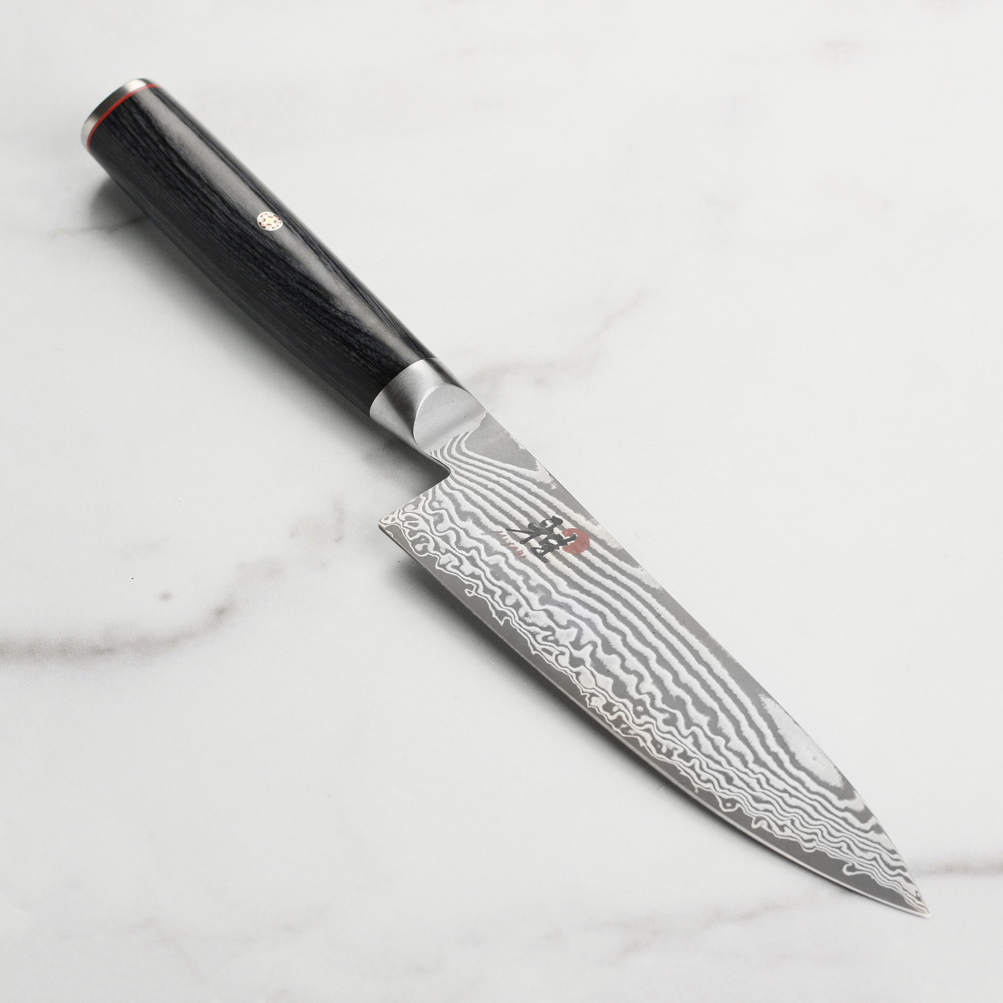 Miyabi Kaizen II 6-inch chef's knife showcasing its Damascus blade and Pakkawood handle from an angled view.