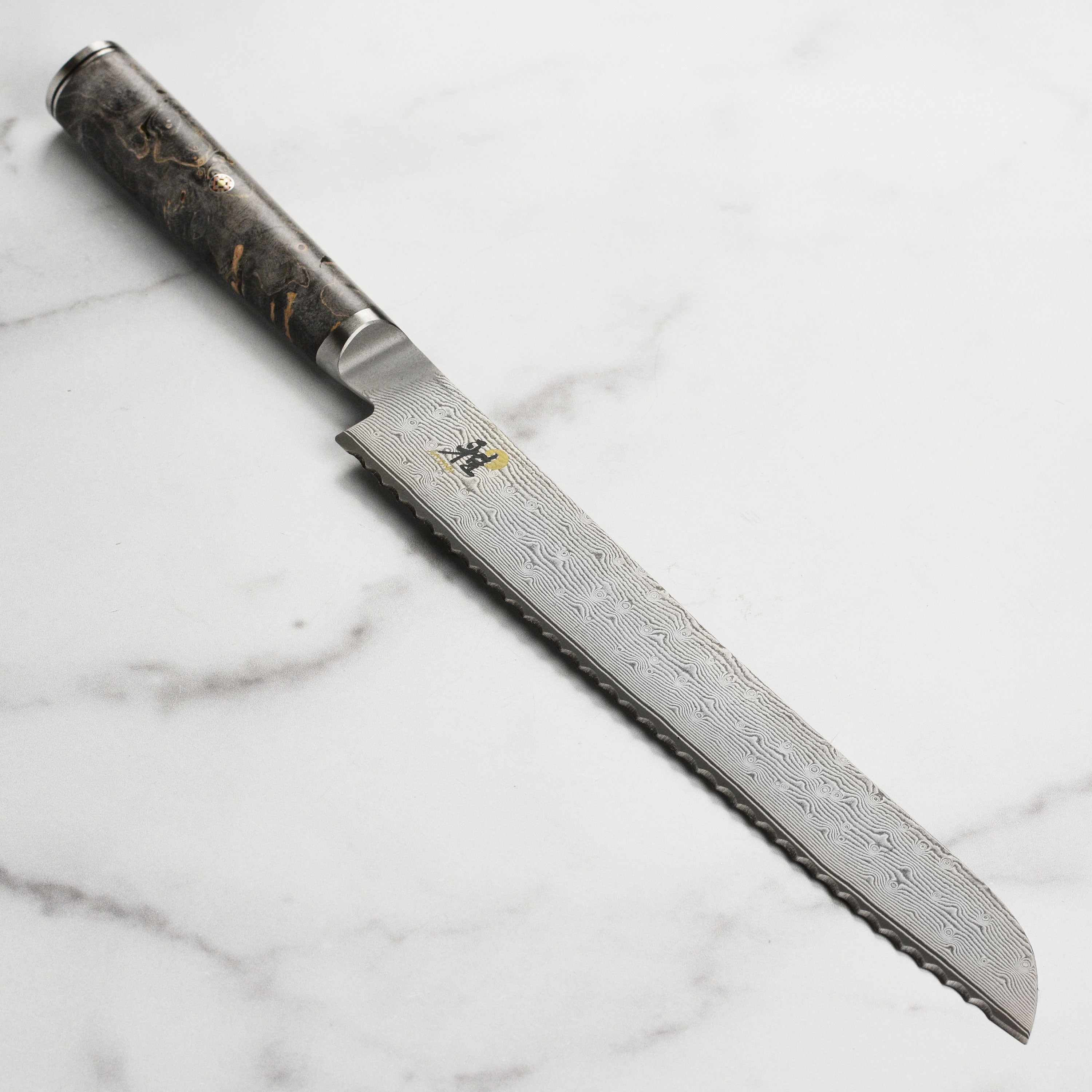 Miyabi Black 9-Inch Damascus Bread Knife from the side, highlighting the blade's intricate Damascus pattern.