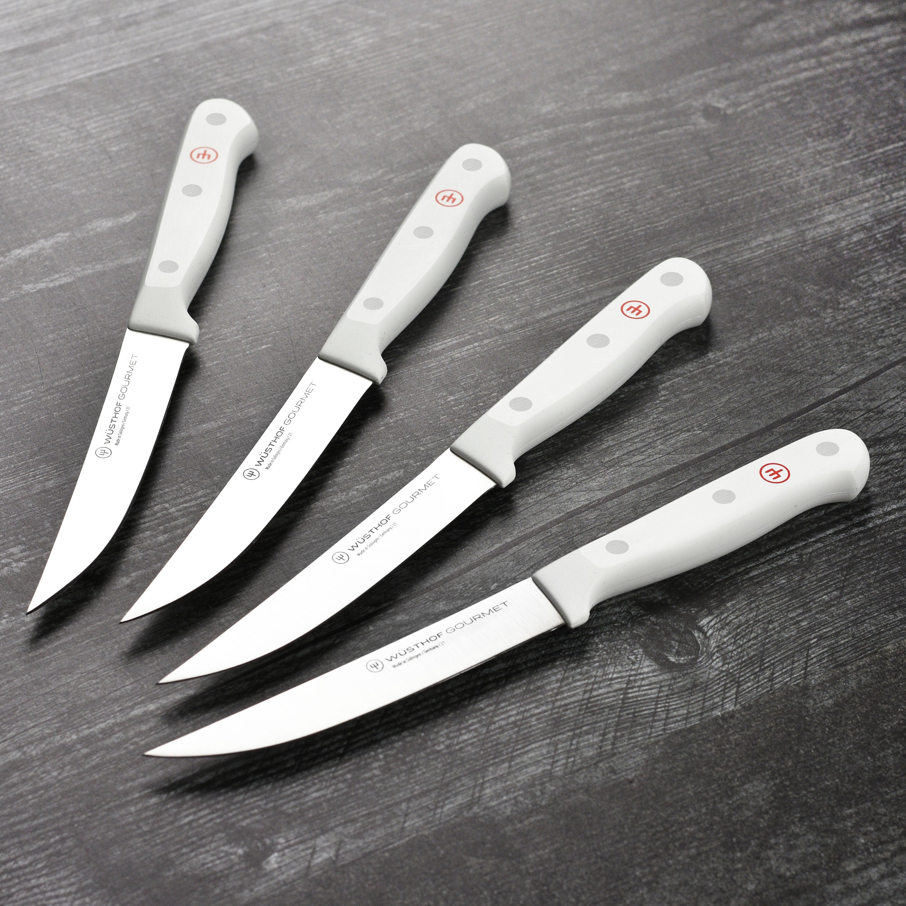 Wusthof Gourmet steak knife set with white handles displayed on a wooden table.