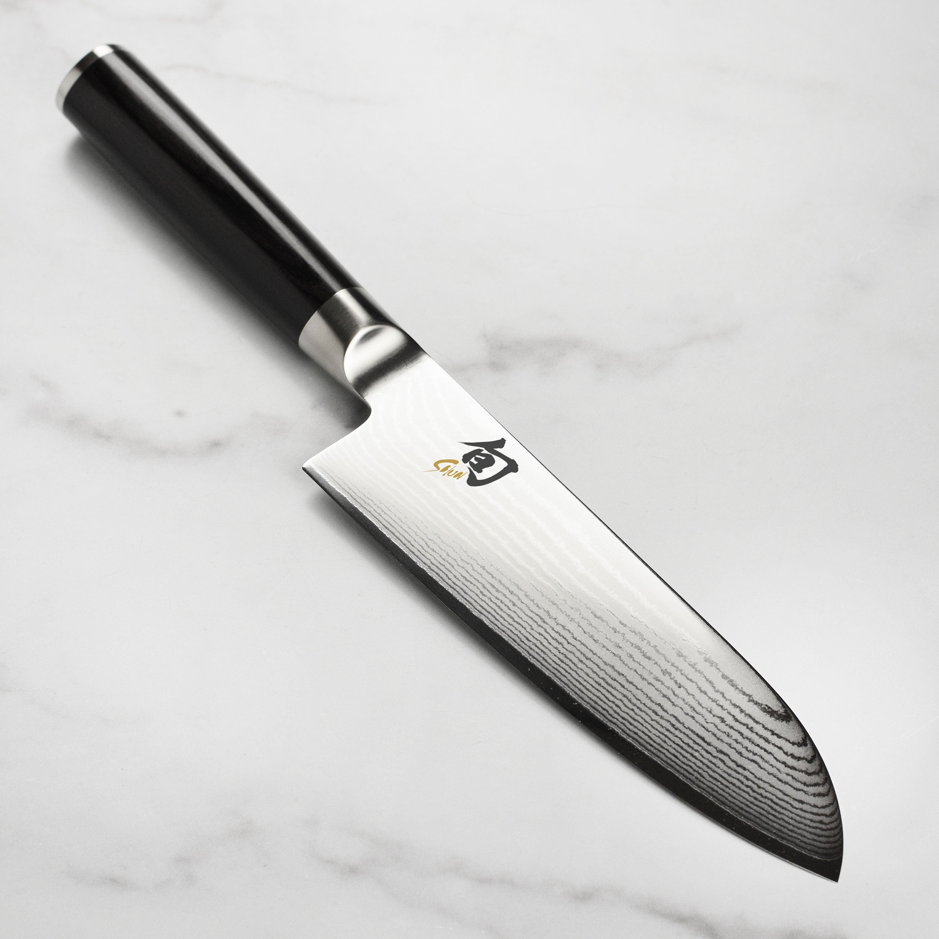 Handcrafted Japanese Santoku knife with Damascus layered blade and ebony handle, angled for slicing