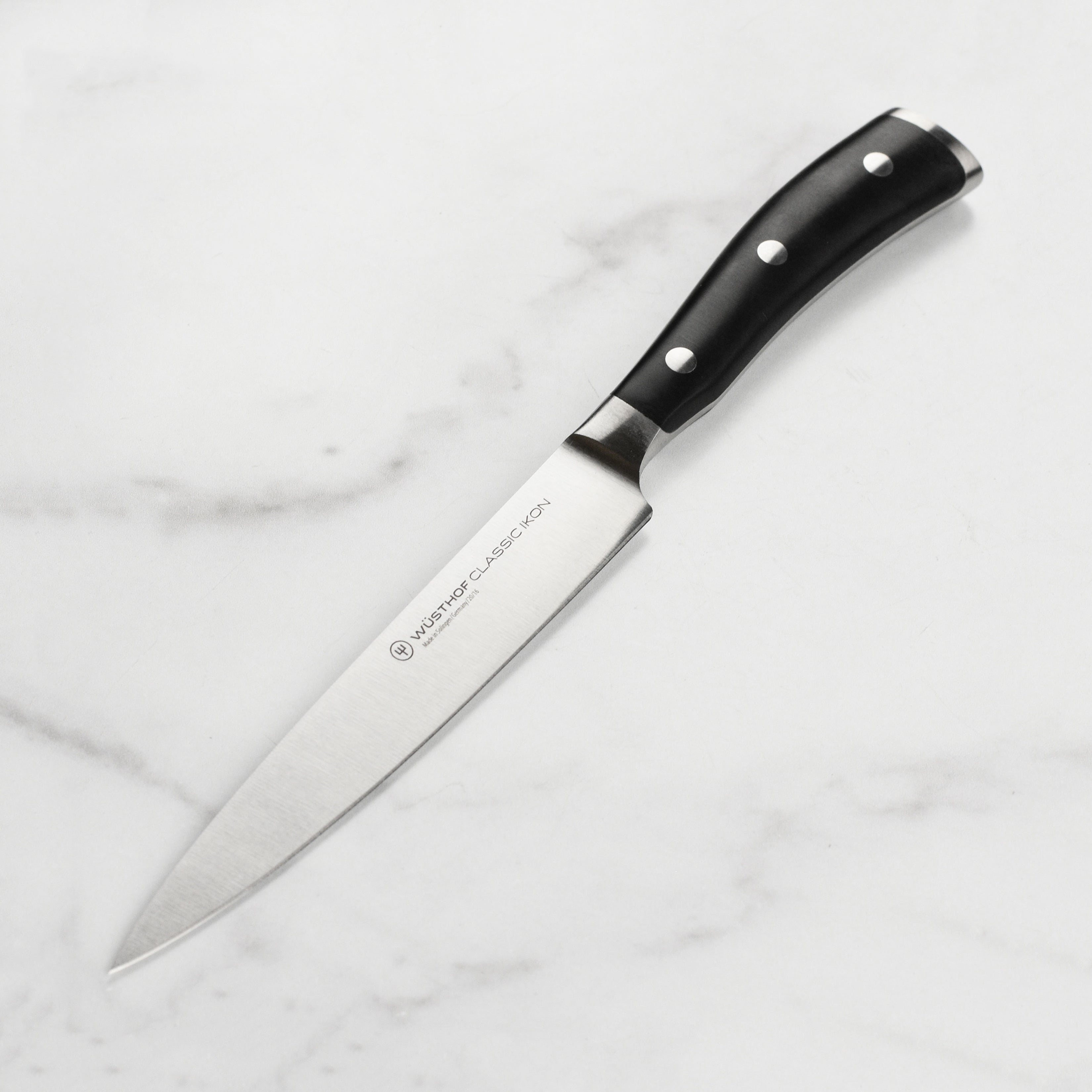 Wusthof Classic Ikon utility knife showcasing its sharp blade and ergonomic handle from a side angle.