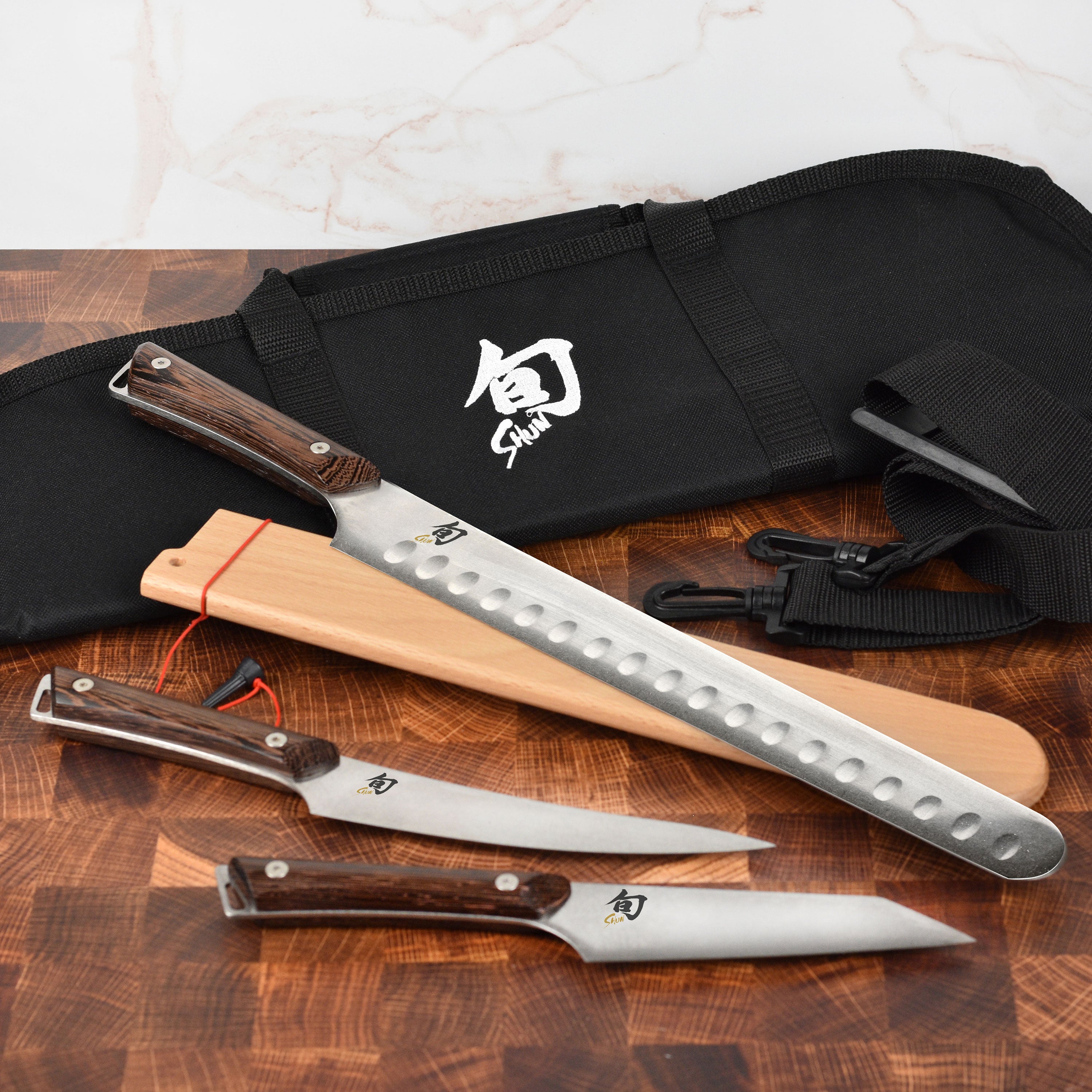 Overhead view of Shun Japanese BBQ knives displayed on a wooden board, showing blade texture and tagayasan wood handles.