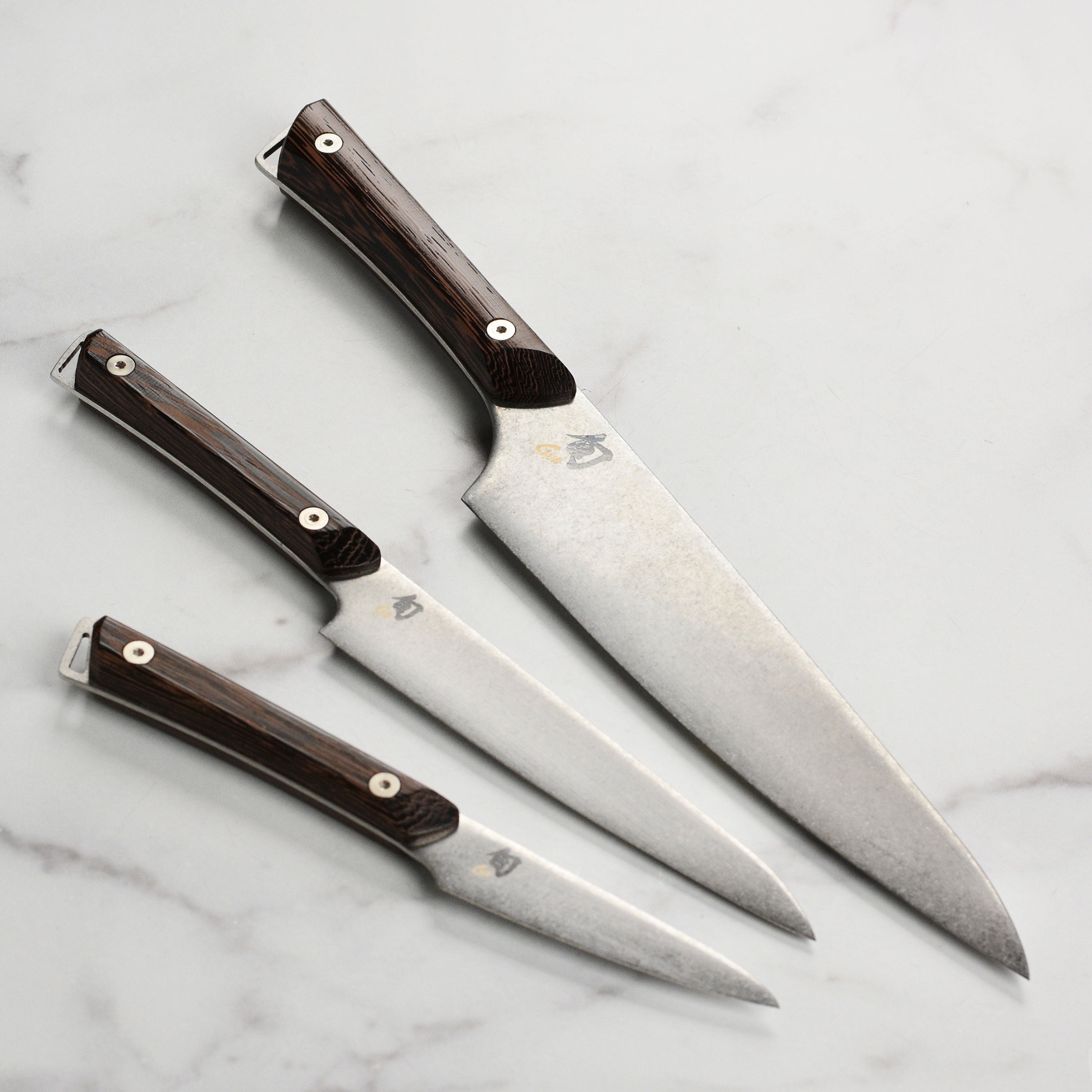 Overhead view of the Shun Kanso knife set arranged on a walnut cutting board with fresh herbs, showcasing handcrafted blade finish