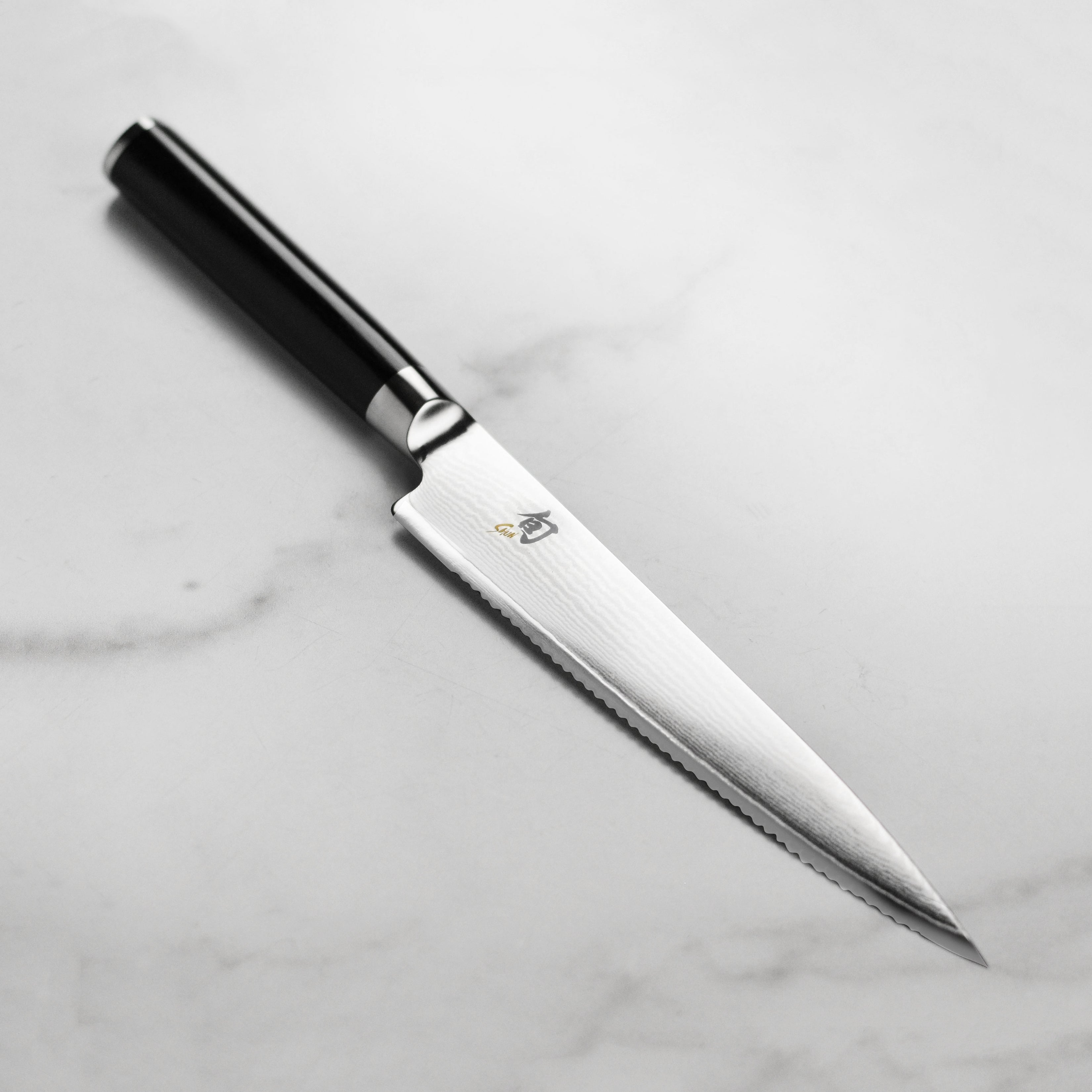 Close-up of Shun Classic 6-Inch Serrated Kitchen Knife highlighting the Damascus cladding and sharp serrated edge.