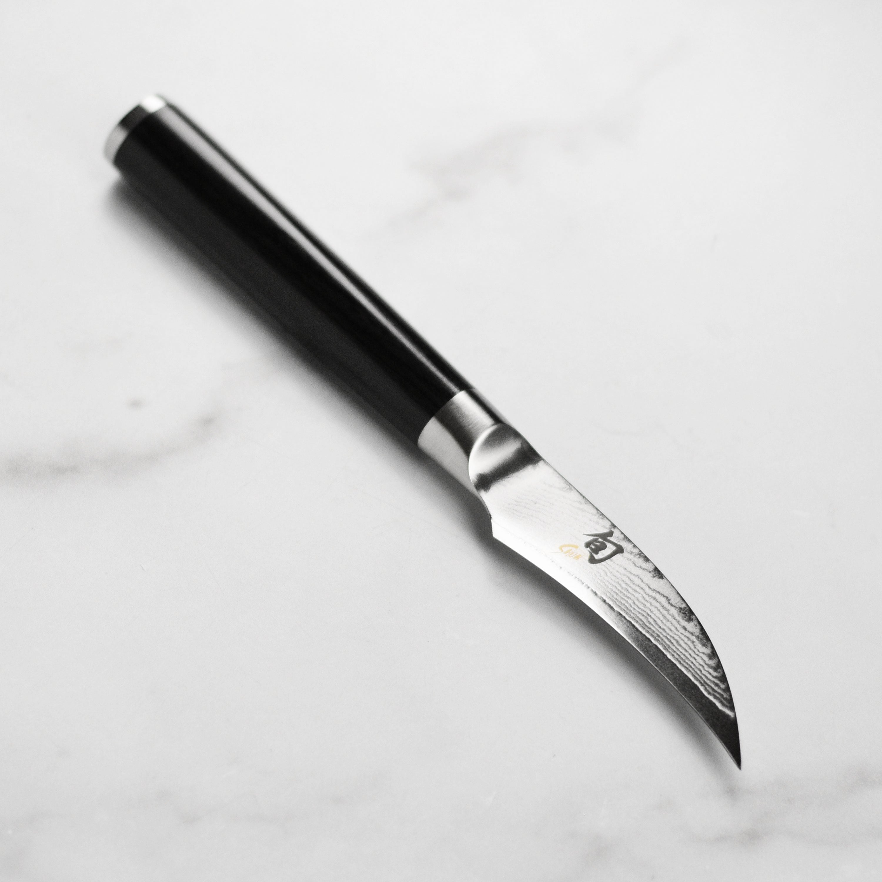Close-up of the Shun Classic peeling knife blade showing its Damascus layering and curved edge