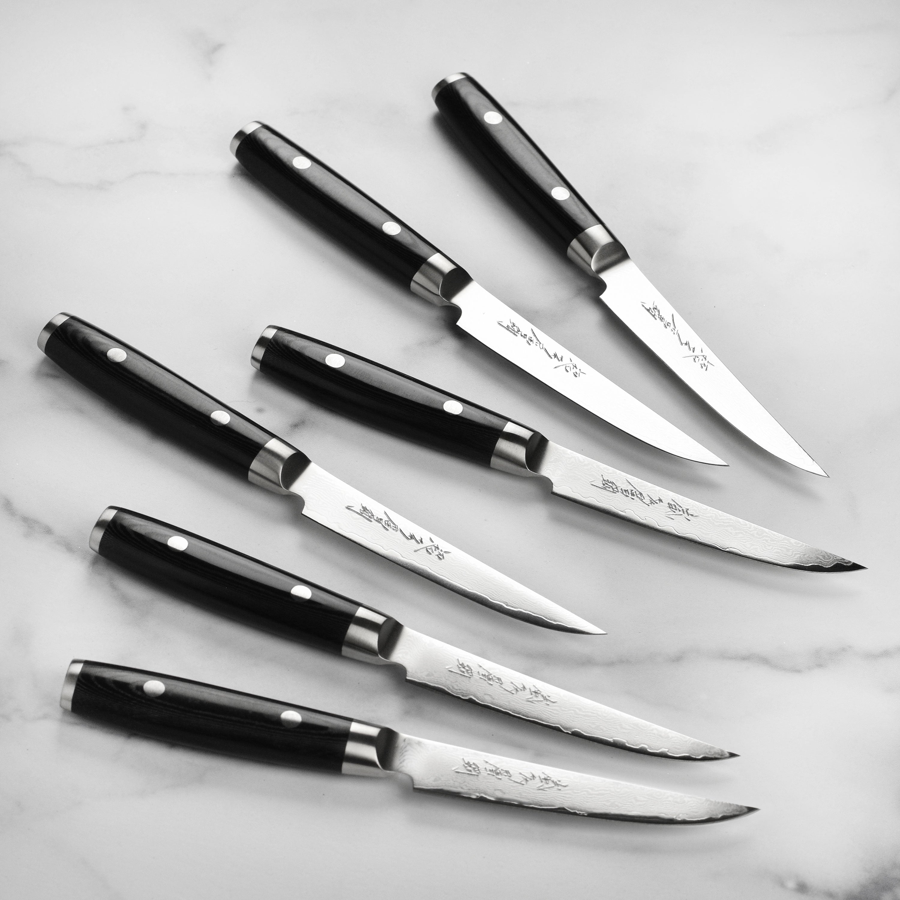 Yaxell Ran Plus steak knives with Damascus steel design on a cutting board