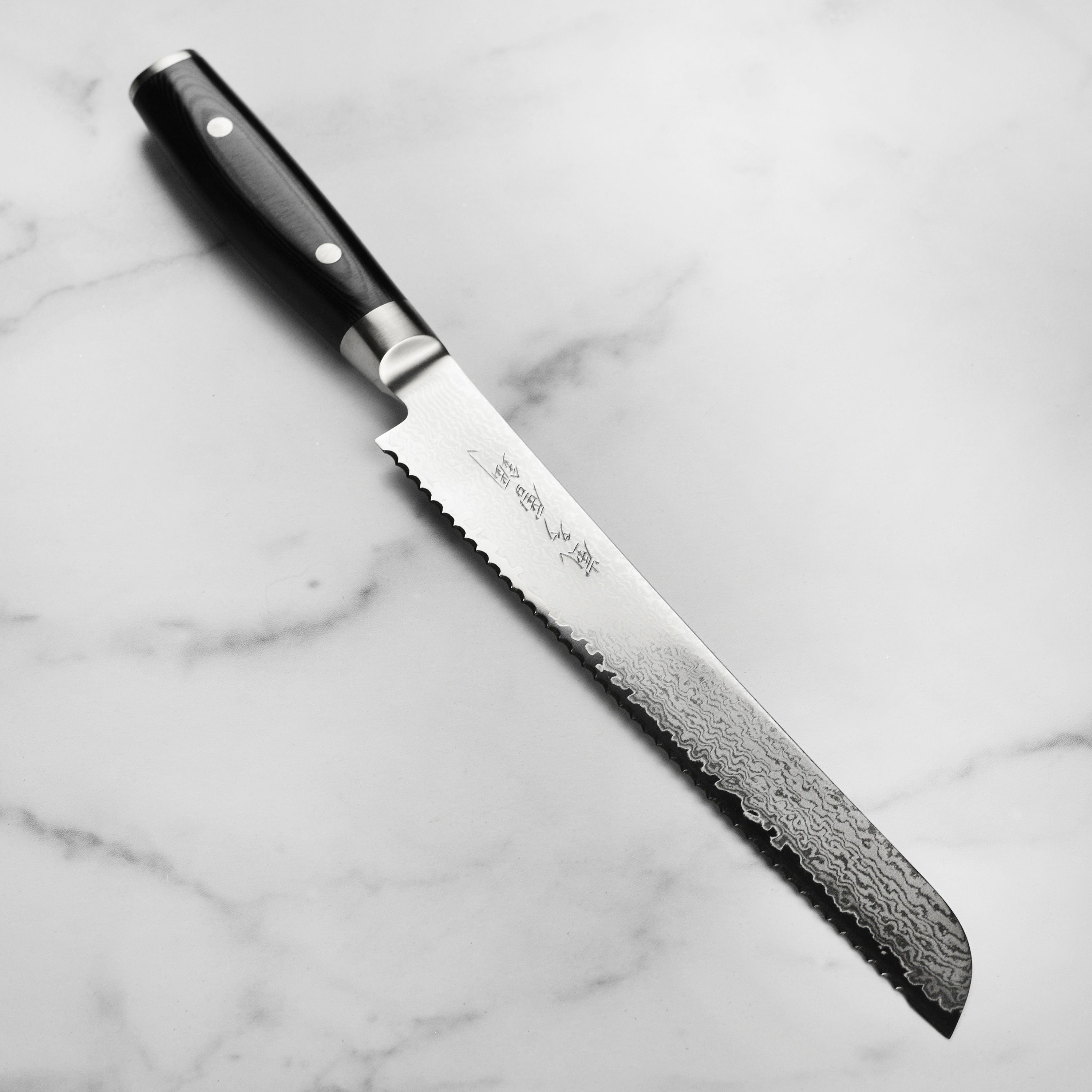 Close-up of Yaxell Ran Plus VG10 bread knife blade showing Damascus layers and engraved kanji