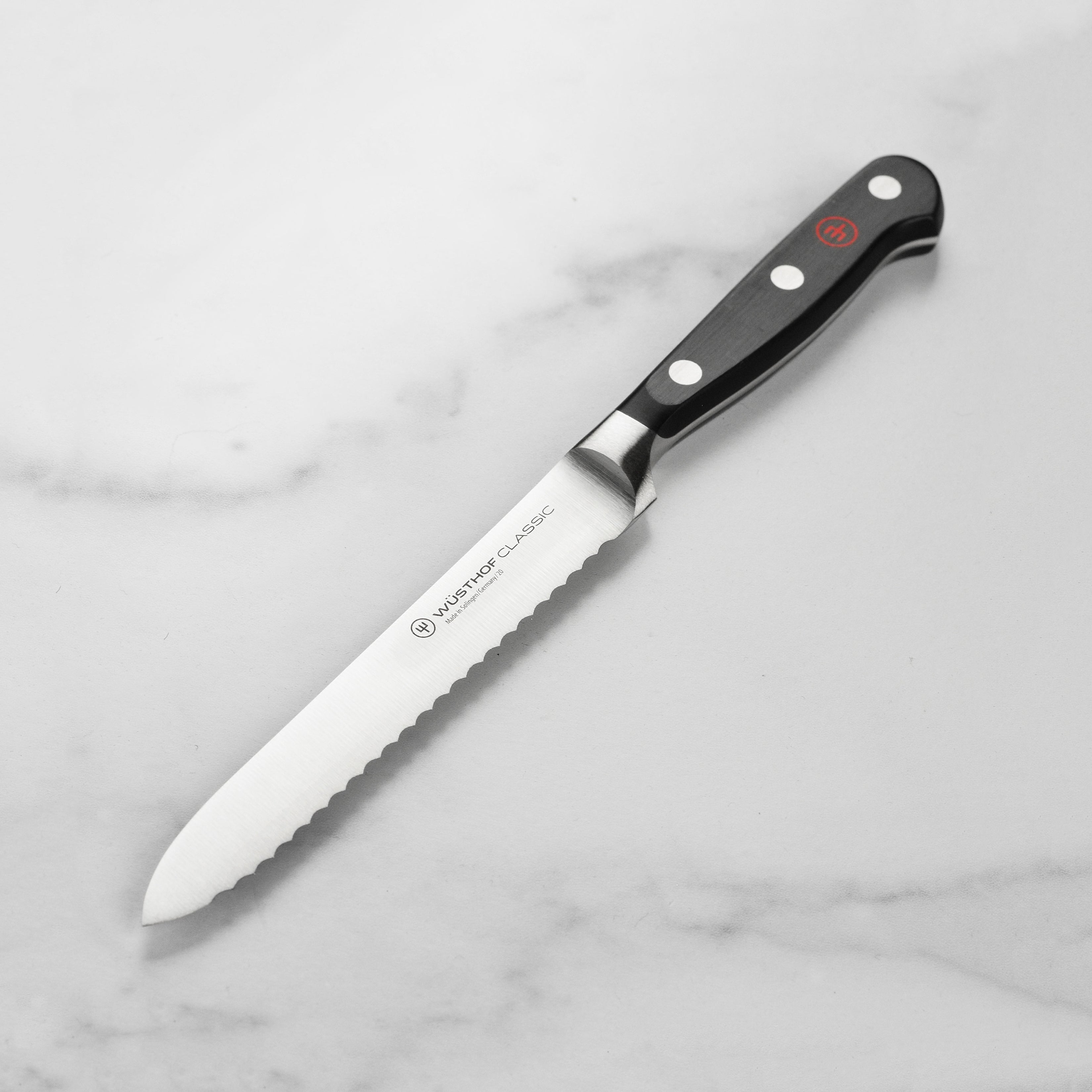 Wusthof Classic 5-Inch Serrated Utility Knife angled view, highlighting its sharp blade and ergonomic handle.