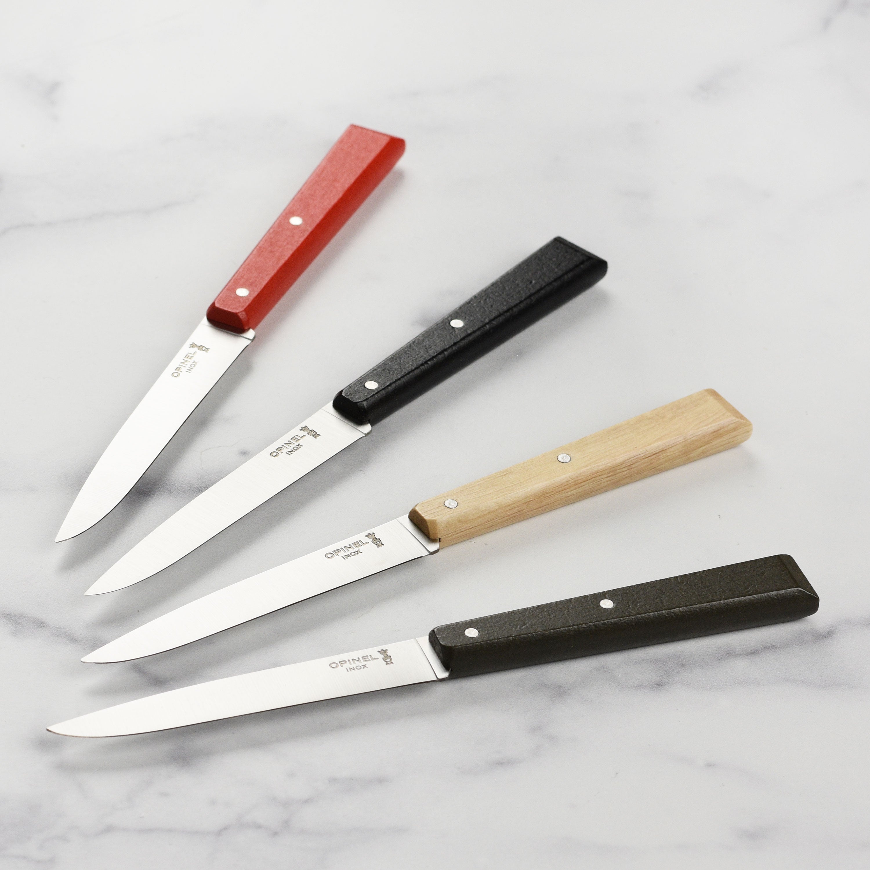 Colorful Opinel steak knives with wooden handles on a dining table.