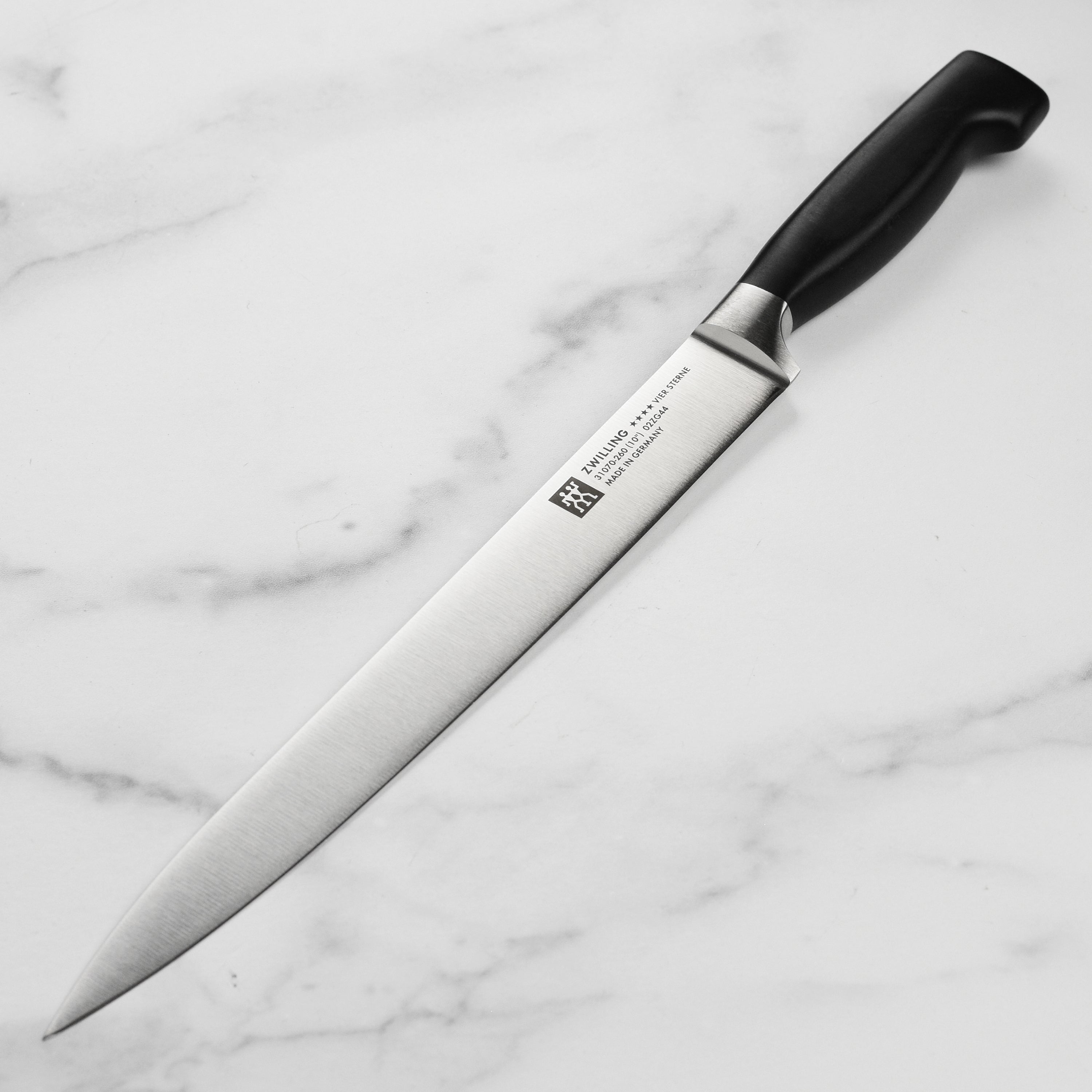 Side view of the Zwilling Four Star 10-inch slicing knife on a wooden cutting board, demonstrating its sharp blade and ergonomic handle.