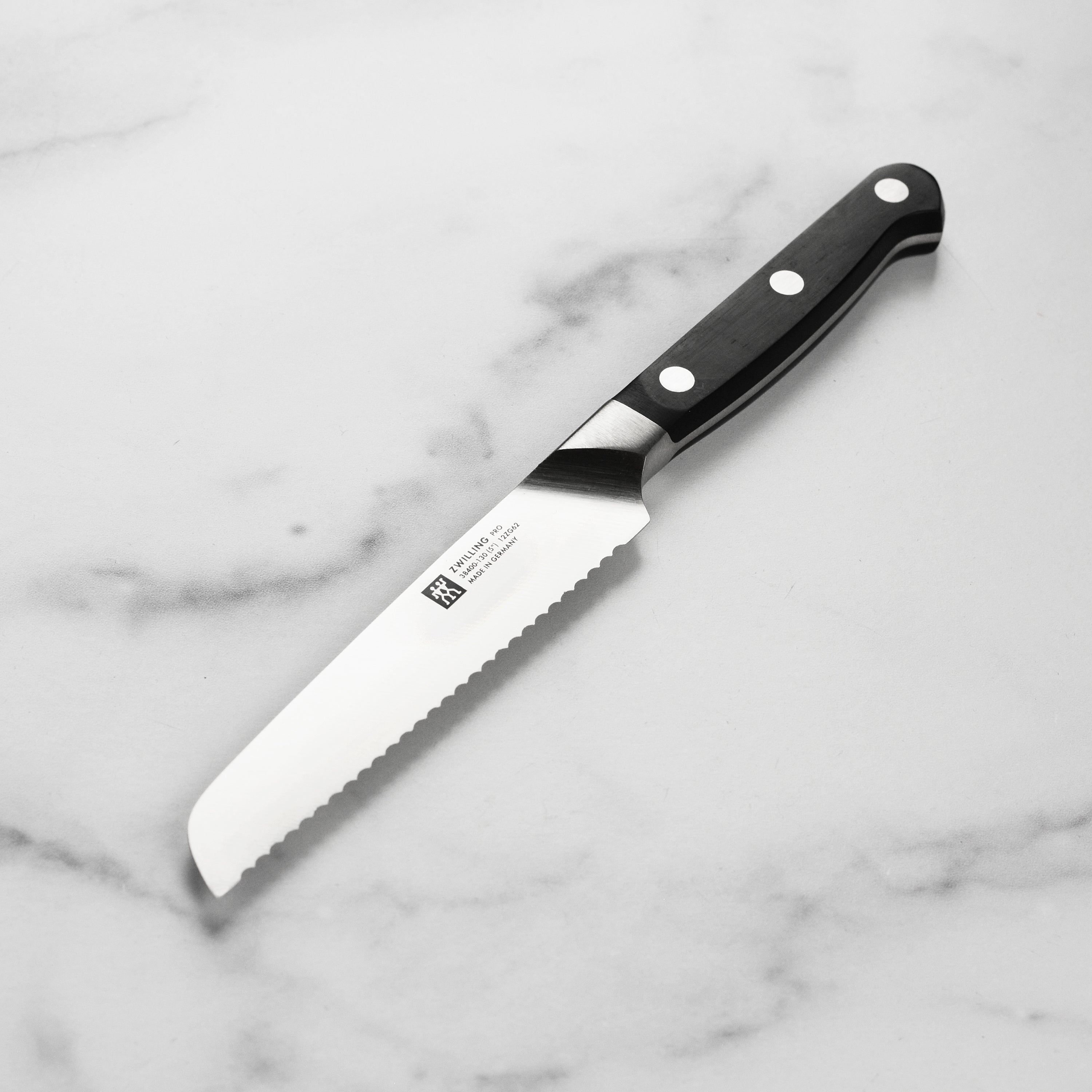 Zwilling Pro 5-inch serrated utility knife displayed on a cutting board.