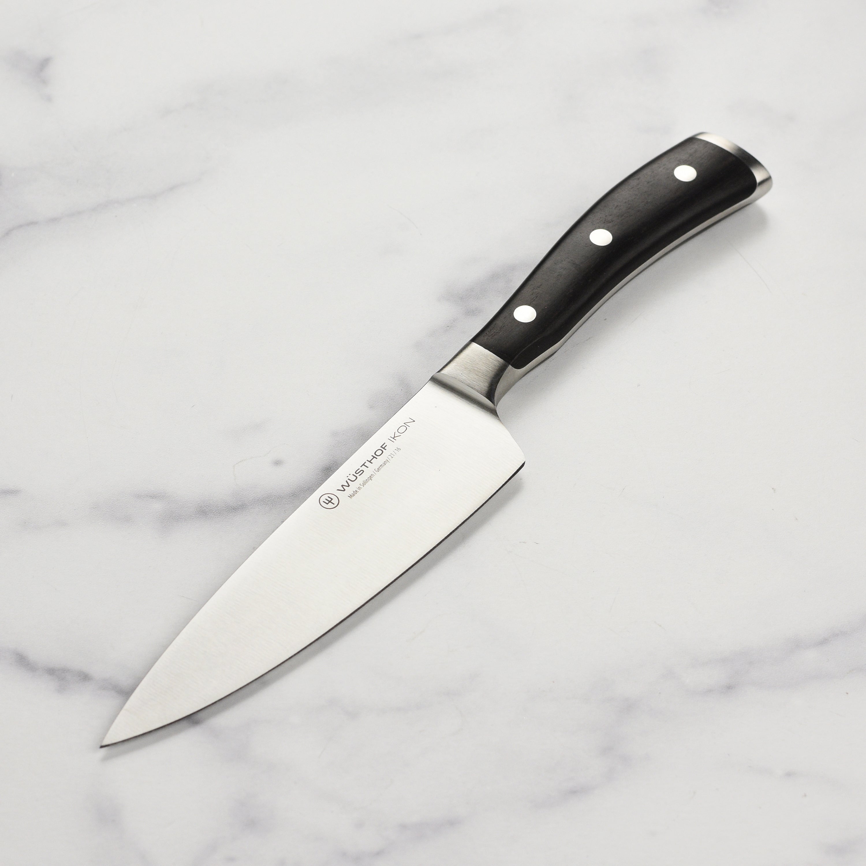 Wusthof Ikon Blackwood chef's knife resting on a wooden cutting board, emphasizing its ergonomic handle and sharp blade.