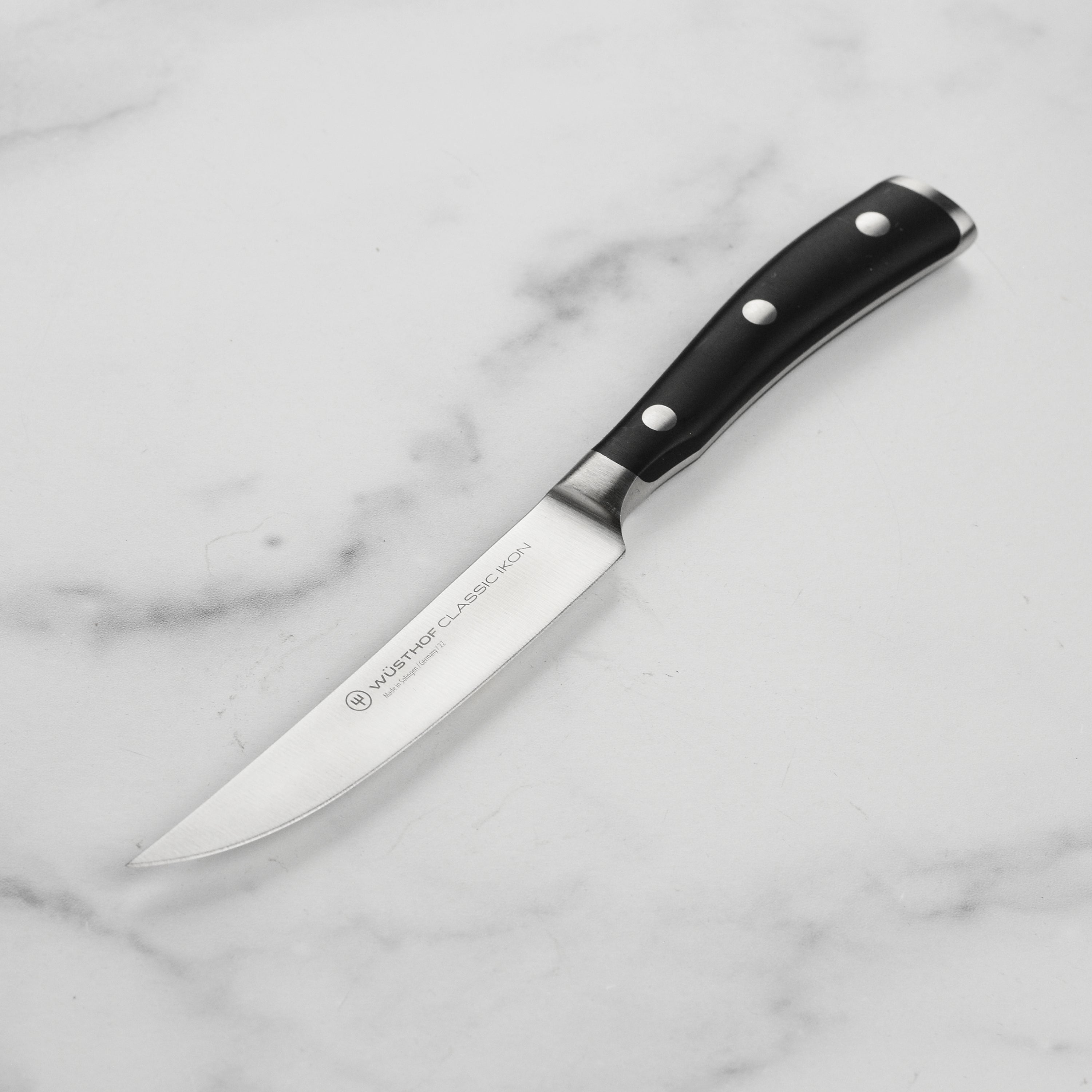 Wusthof Classic Ikon 4.5-Inch steak knife on a wooden cutting board, showcasing its sharp blade and ergonomic handle.