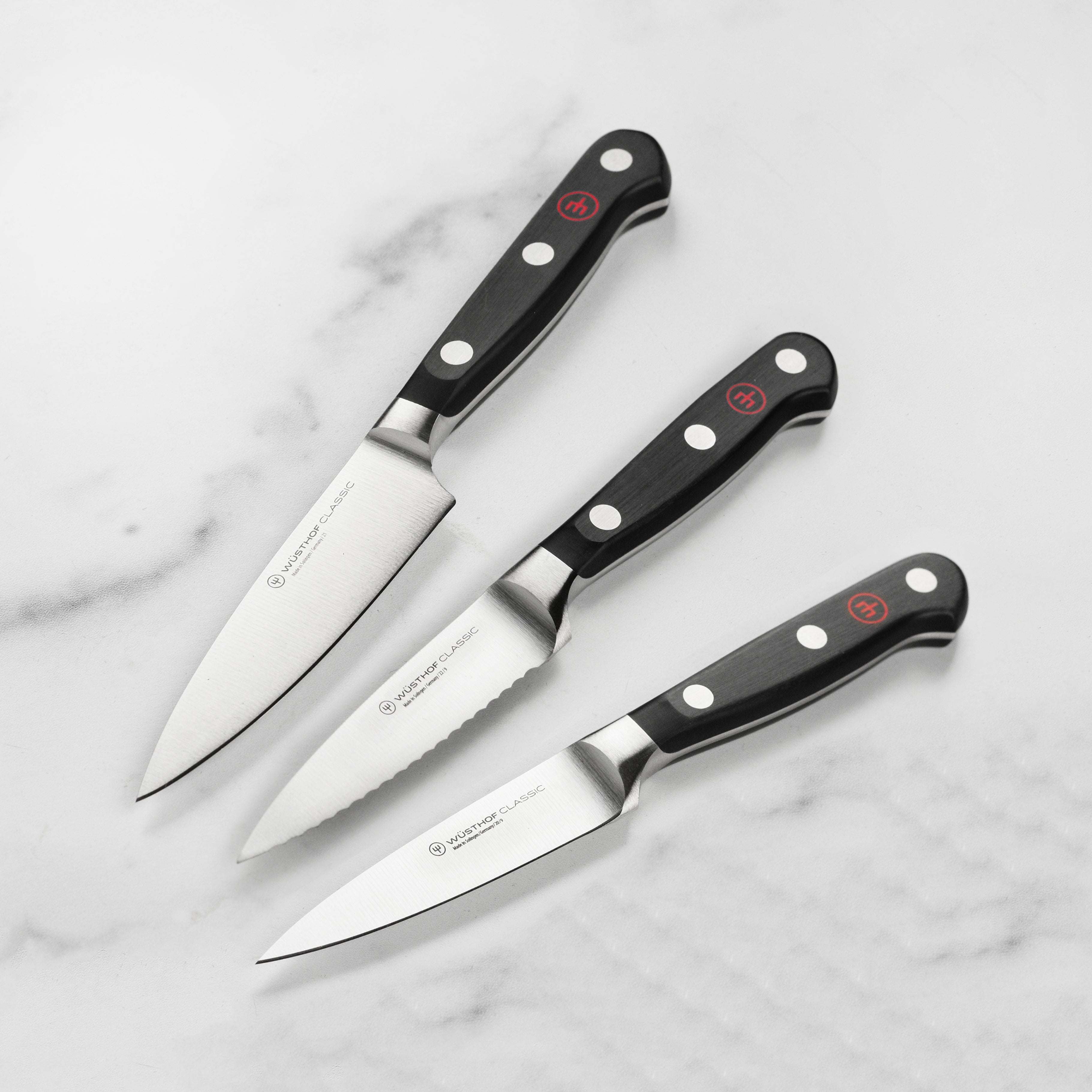 Wusthof Classic Paring Knife Trio displayed on a wooden cutting board.
