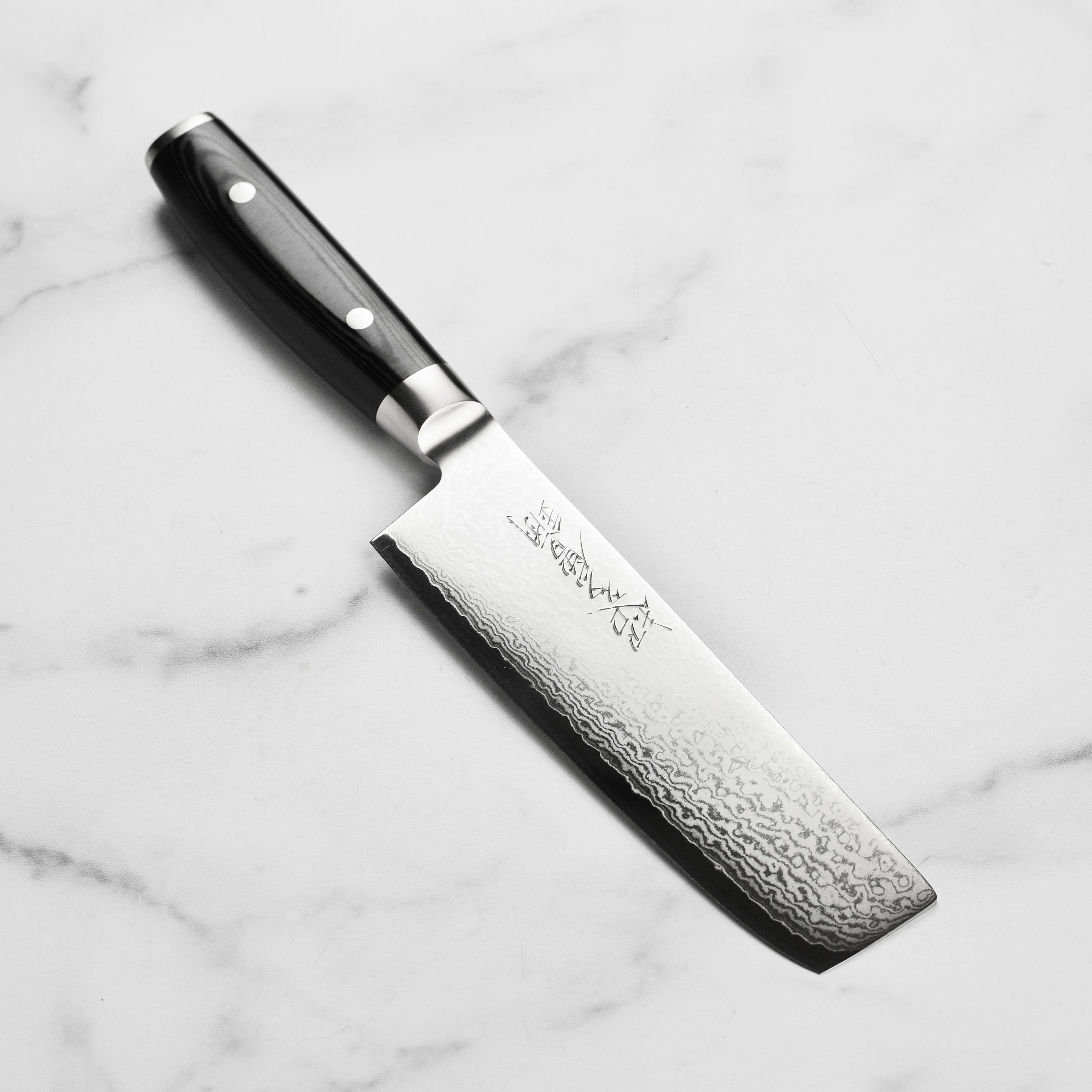 Close-up of the Yaxell Ran Plus Nakiri knife blade highlighting the Damascus pattern and sharp edge.