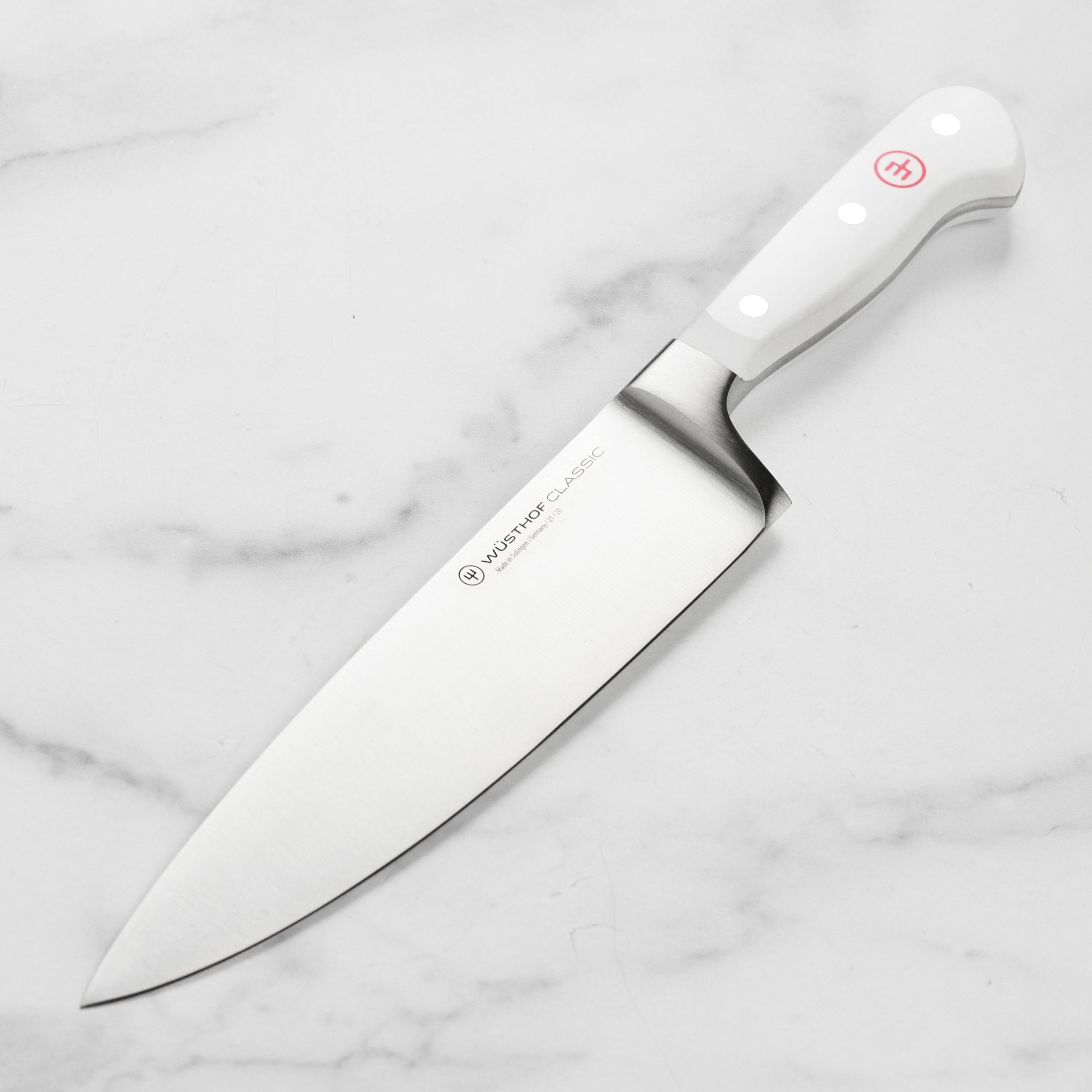 Overhead shot of Wusthof Classic White 8 inch knife slicing fresh herbs on a butcher block
